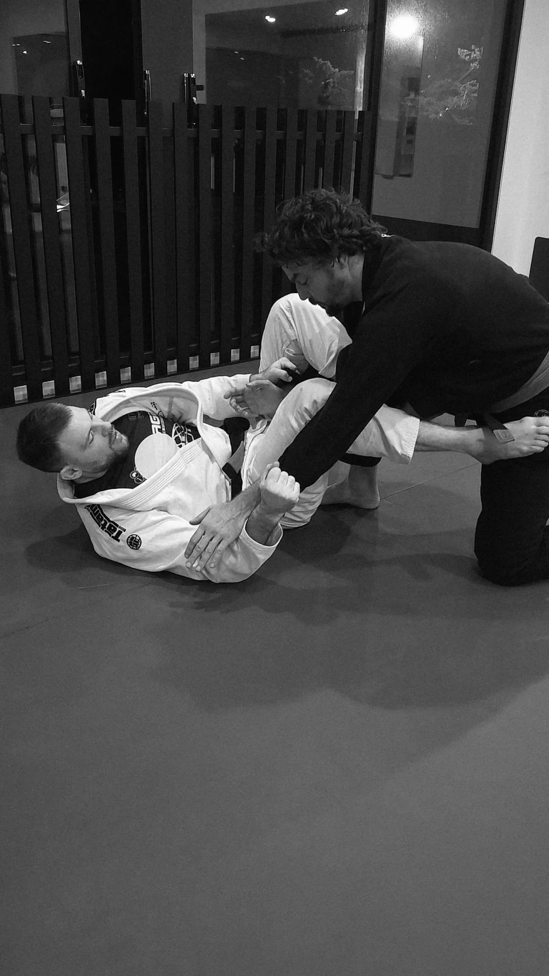 Two men practicing Brazilian Jiu-Jitsu on a mat, with one man using a grappling technique while the other is on the ground.