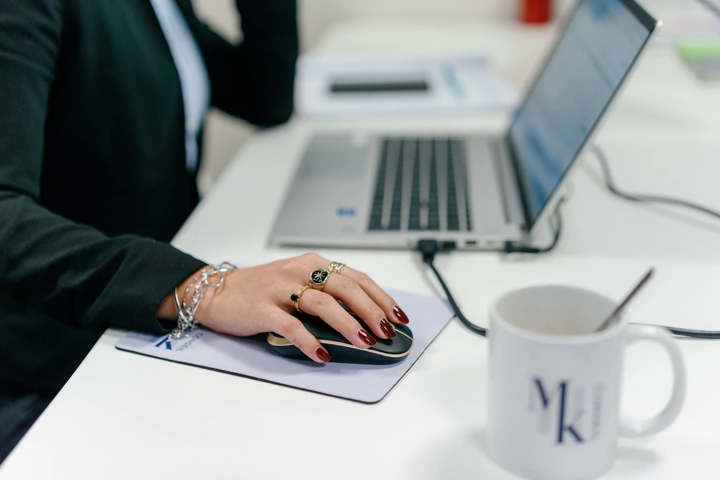 Une personne utilisant une souris d'ordinateur à un bureau avec un ordinateur portable, une tasse, et des accessoires de bureau.