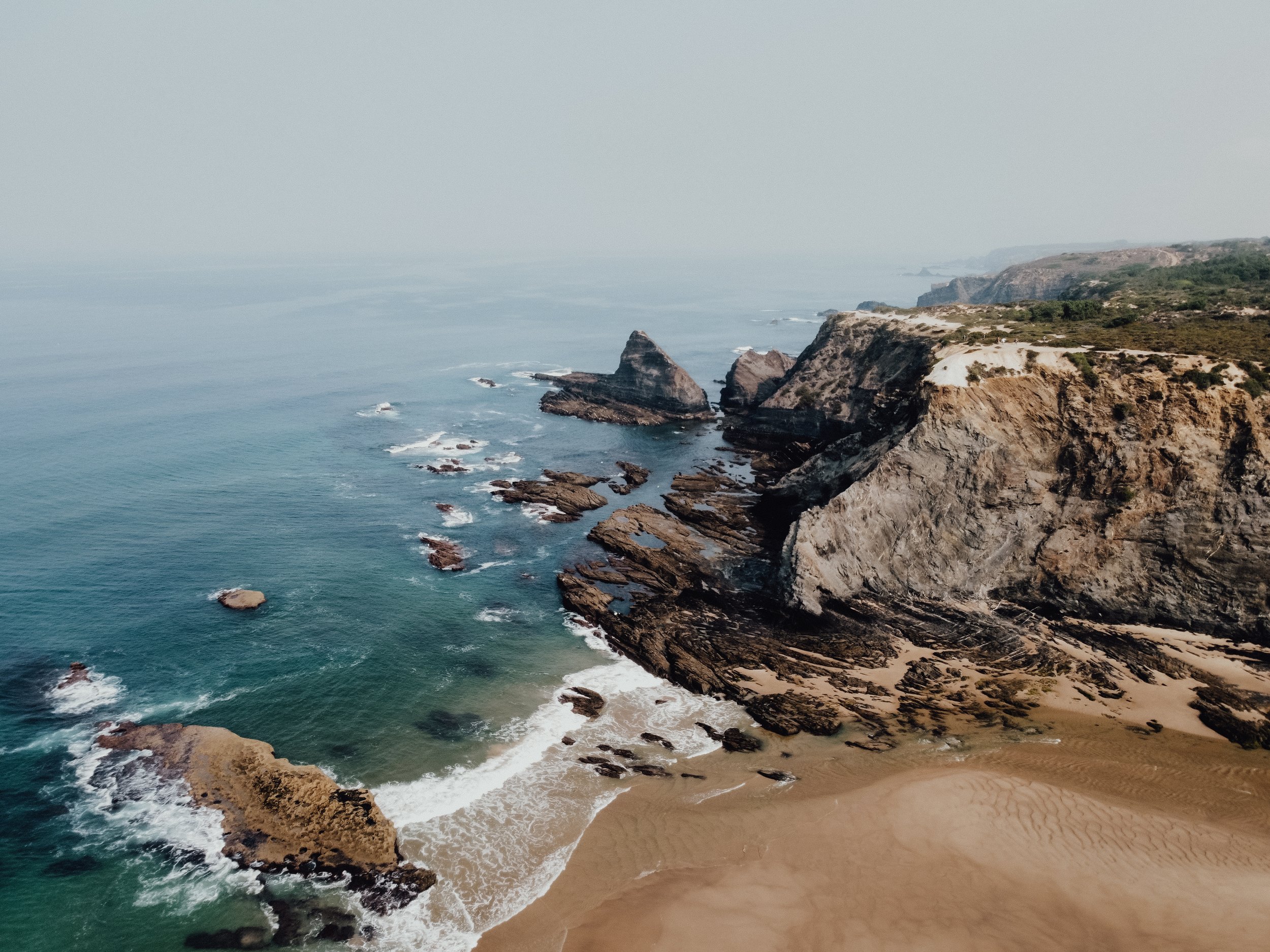 Eine Küstenlandschaft mit Felsen, Sandstrand und Meer, umgeben von Klippen und felsigen Ufern.