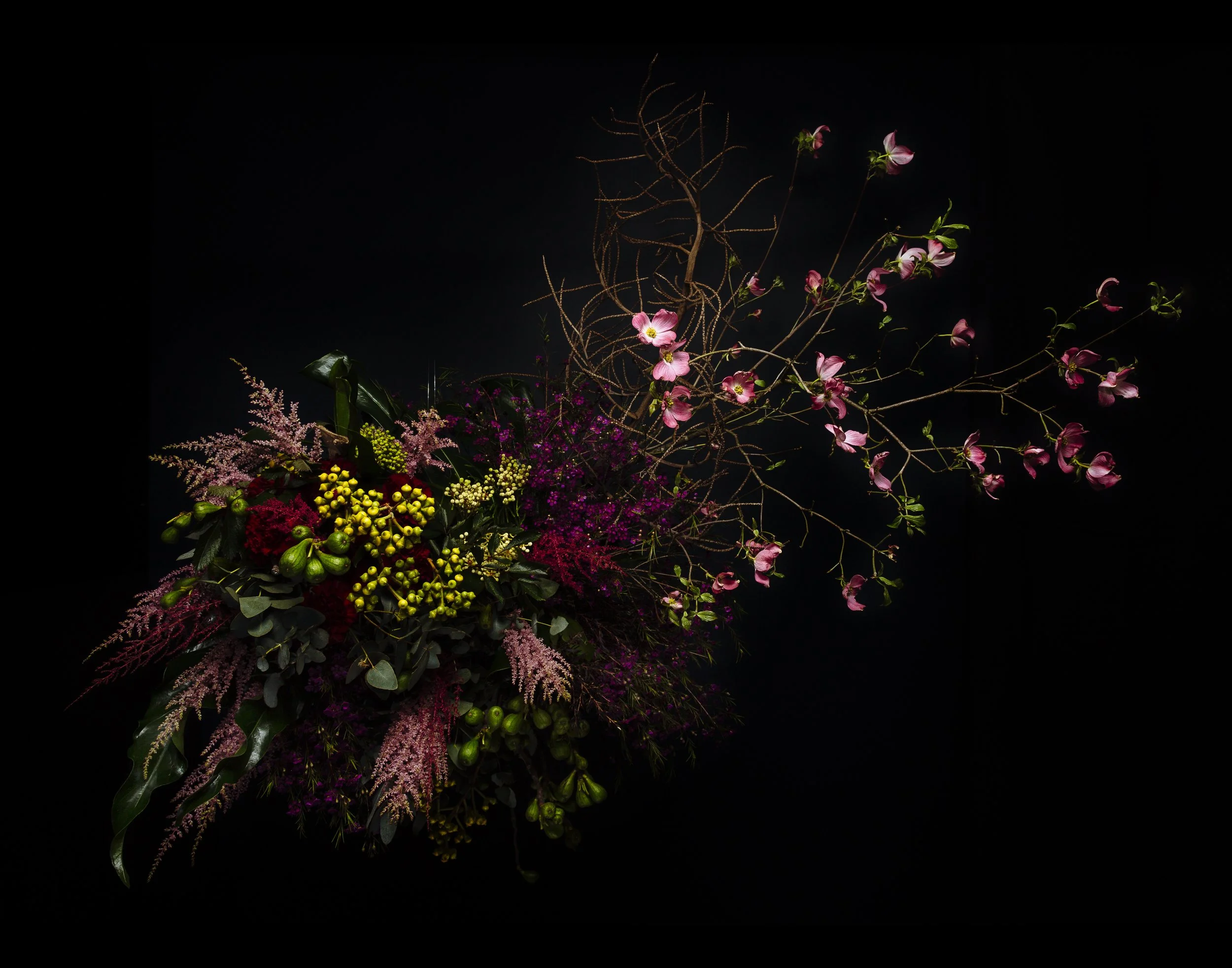A floral arrangement with pink, purple, yellow, and red flowers and greenery against a black background.