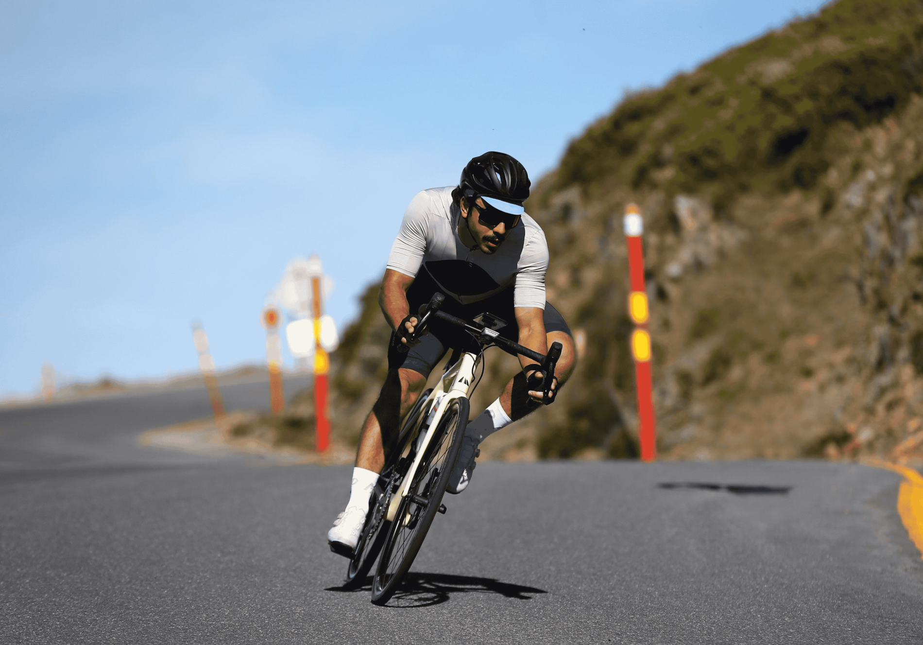Physiotherapist and criterion rider Gianni Chng in athletic gear riding a bicycle on a mountain road, leaning into a turn with a rocky hillside in the background.