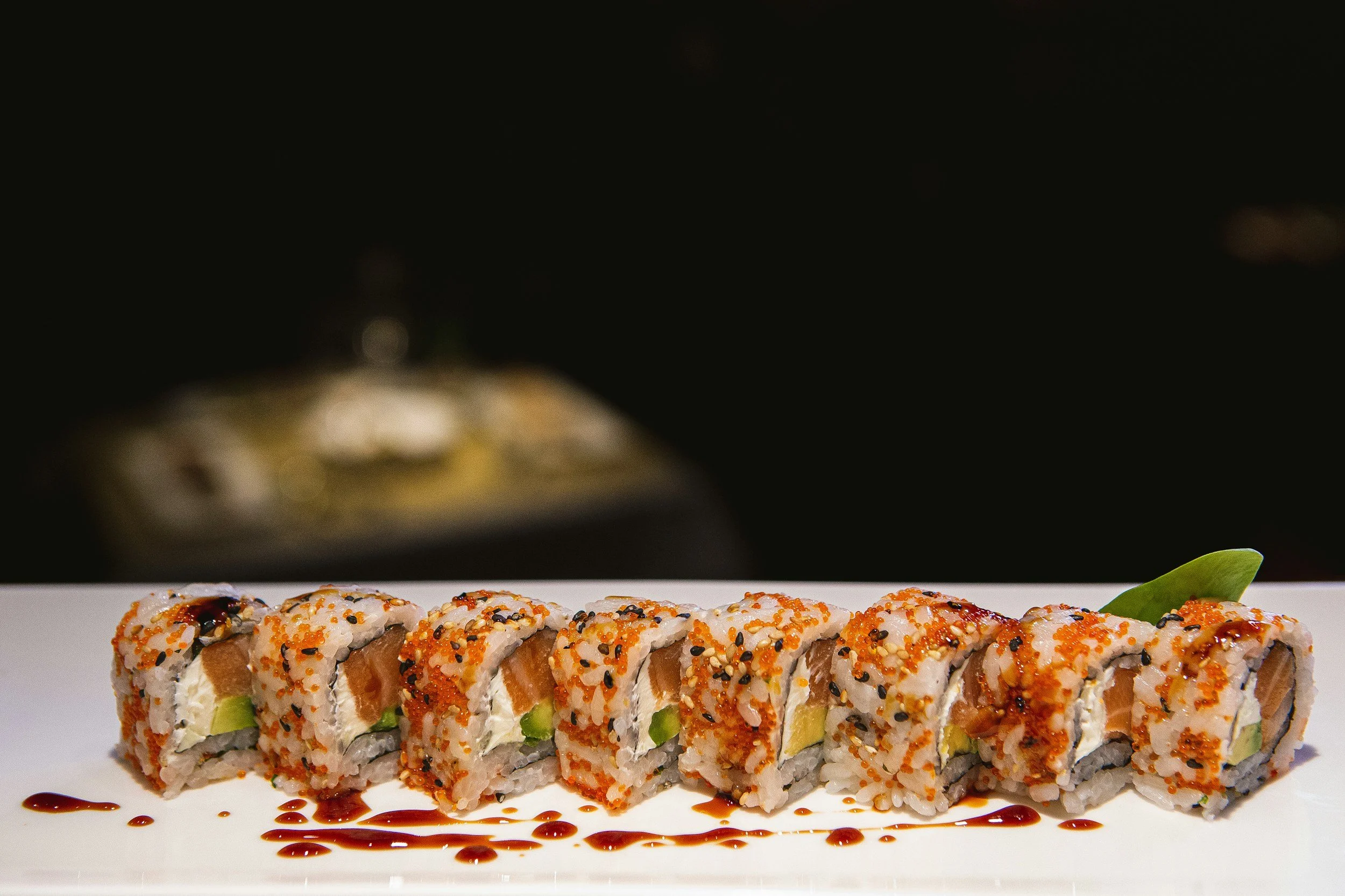 Sushi-rulle med lax, avokado och soja på en vit tallrik.