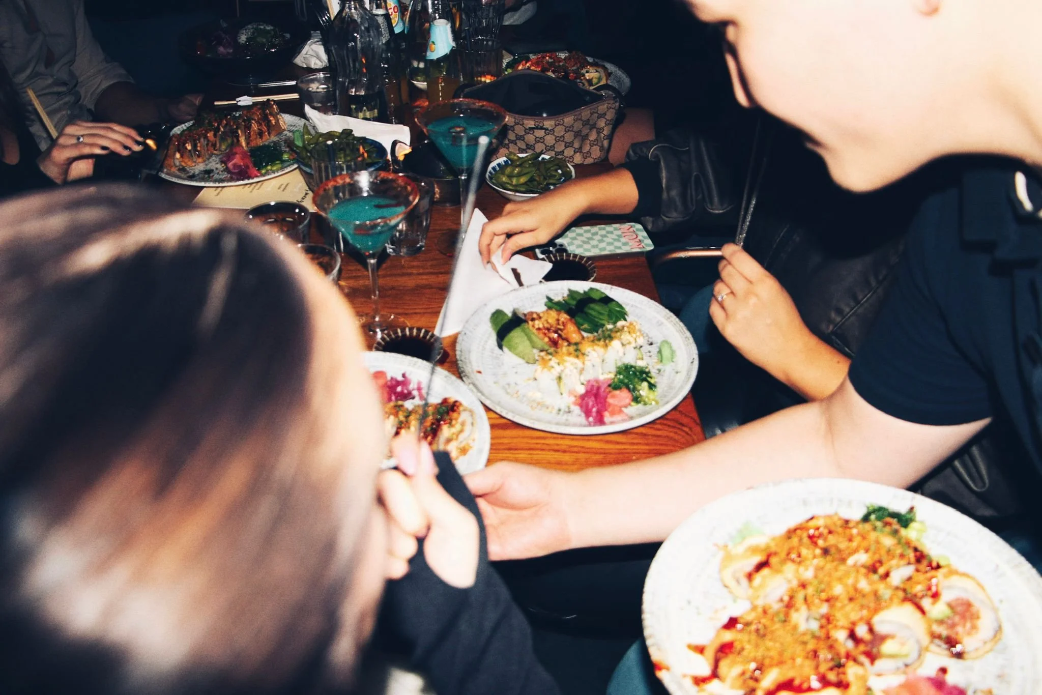 Folk som äter sushi vid ett bord med flera tallrikar och drinkar.