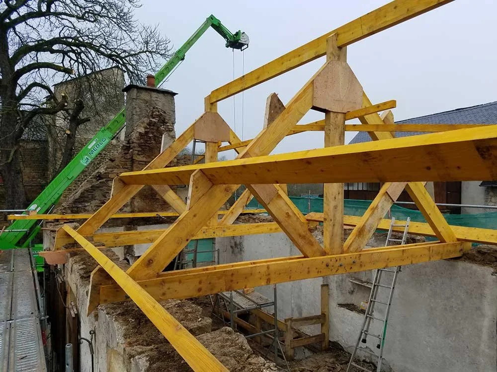 Construction d'une structure en bois avec une grue verte sur un chantier, avec des échelles et des murs en arrière-plan.
