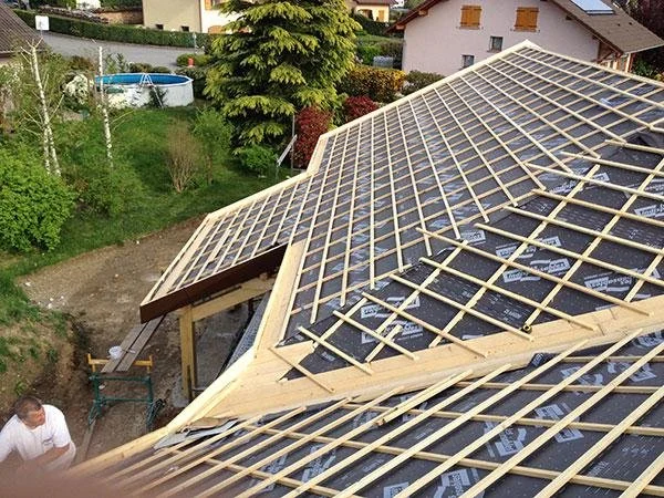 Installation de la charpente d'une toiture en cours, avec des planches en bois posées sur la structure.