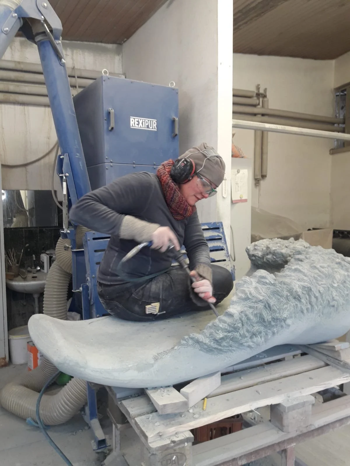 Artisan sculptant une pièce en pierre ou en marbre dans un atelier, portant des protections auditives et des lunettes de sécurité.