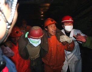 Group of people wearing hard hats, masks, and protective gear inside an industrial or mining setting.