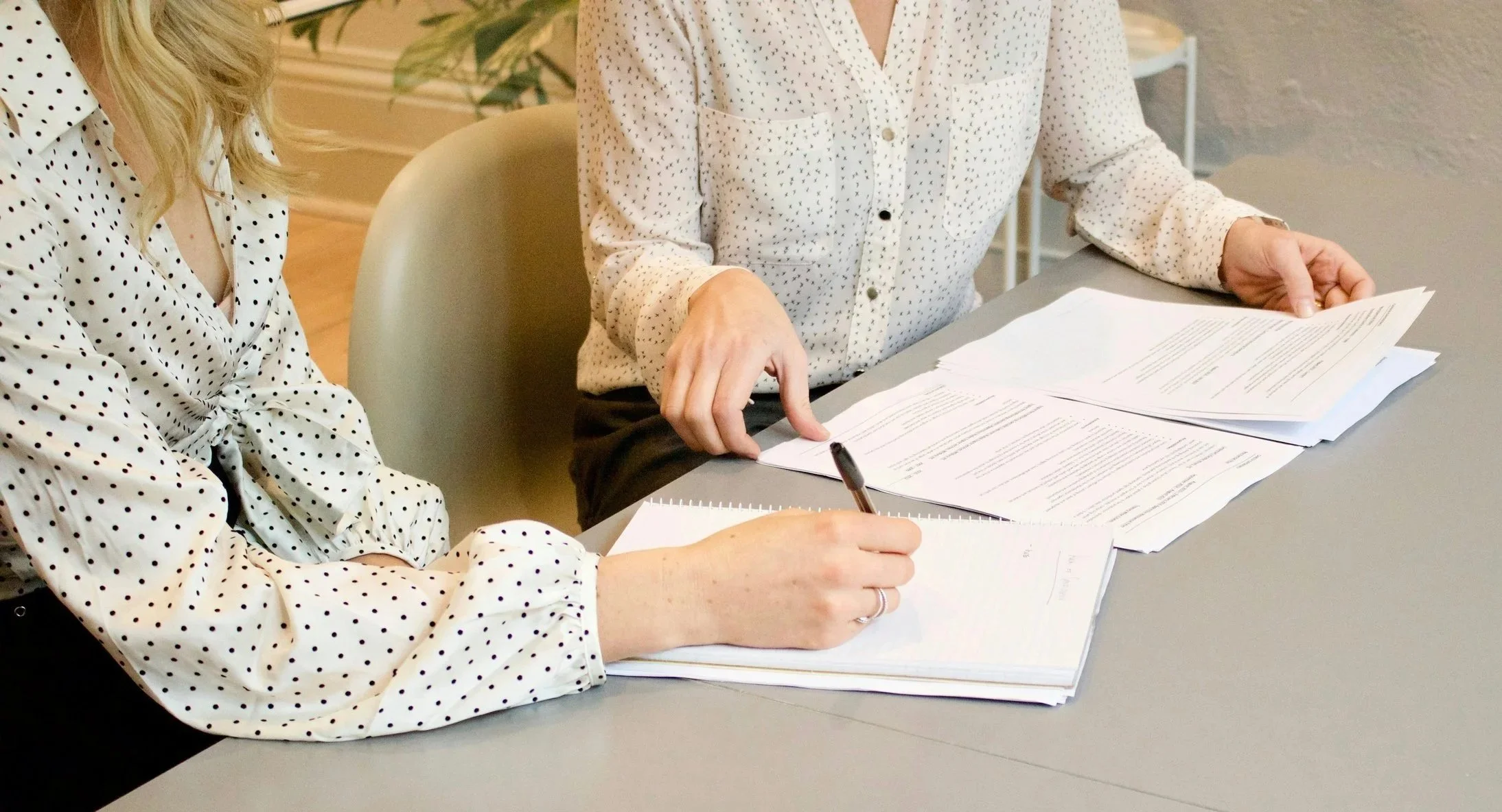 Two women sitting at a desk reviewing documents and taking notes.