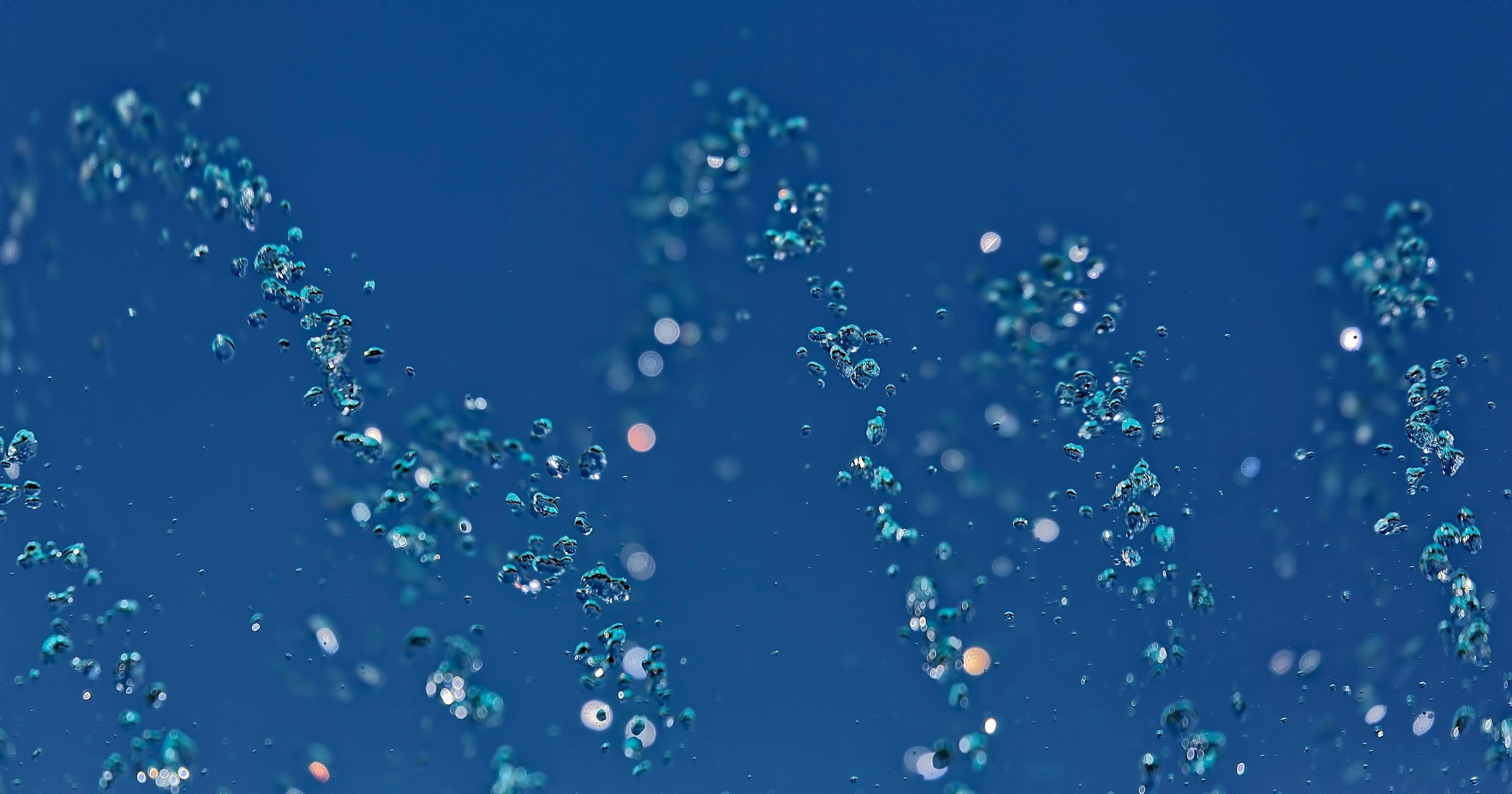 Close-up of water bubbles rising through blue water background.