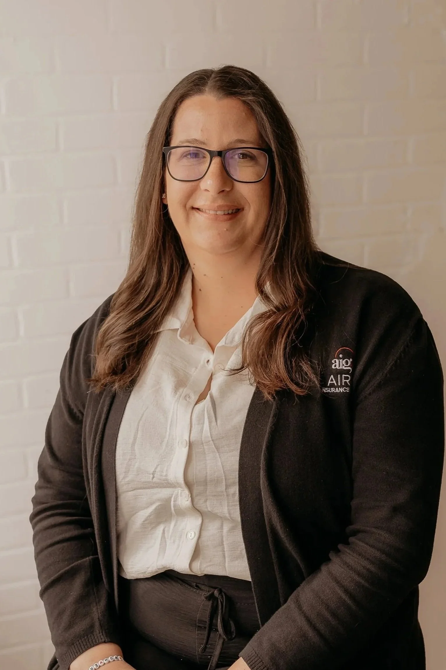 Portrait of a woman with curly brown hair, glasses, and a colorful patterned top, smiling indoors.