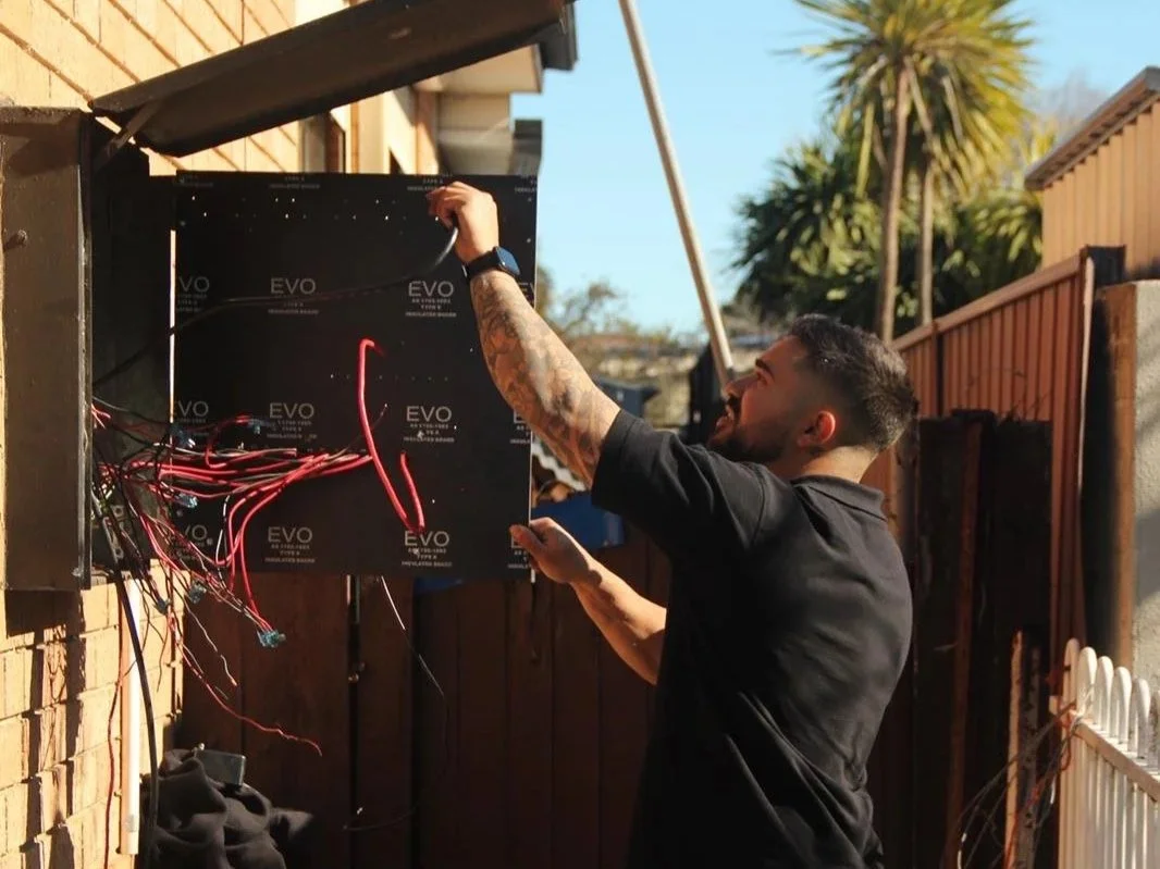 Zamps Electrical technician working on outdoor electrical wiring in a weatherproof box during a residential service call.