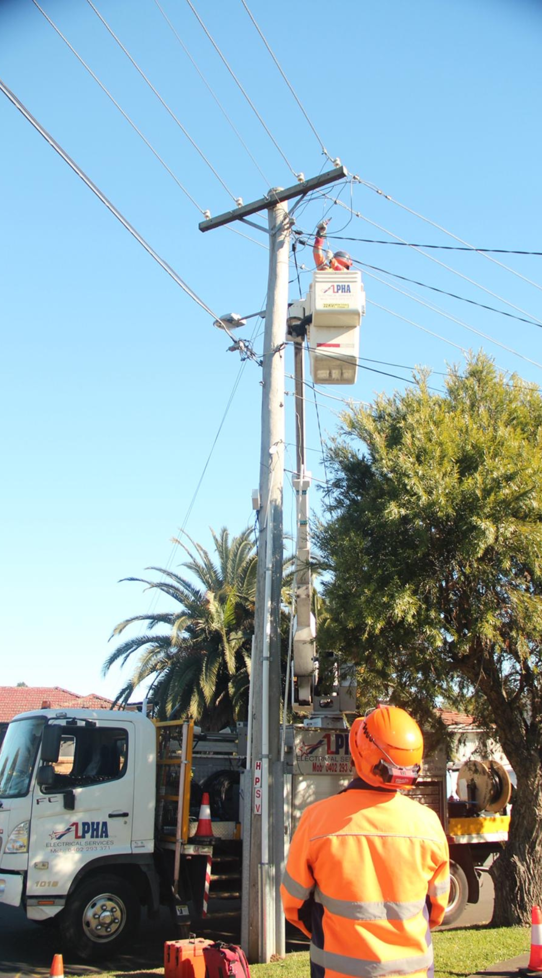 Electrical Level 2 ASP technician working on a utility pole using an elevated bucket, with safety crew and truck on site.