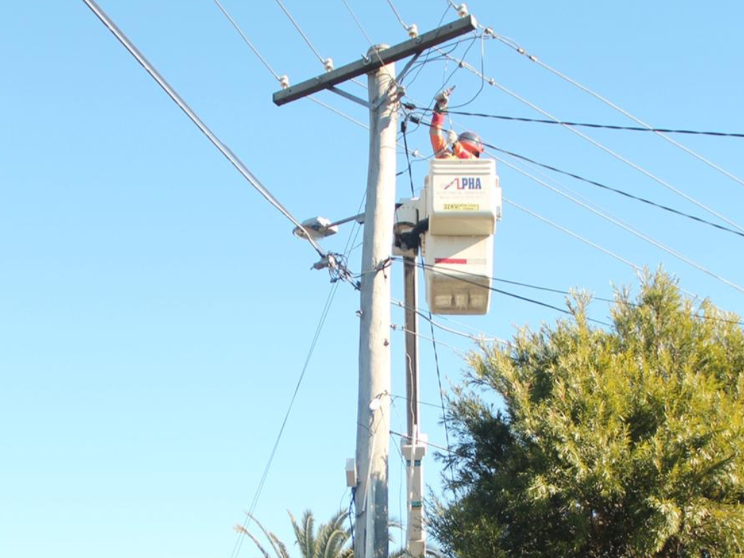 Electrical technician in safety gear repairing electrical wiring on a utility pole.