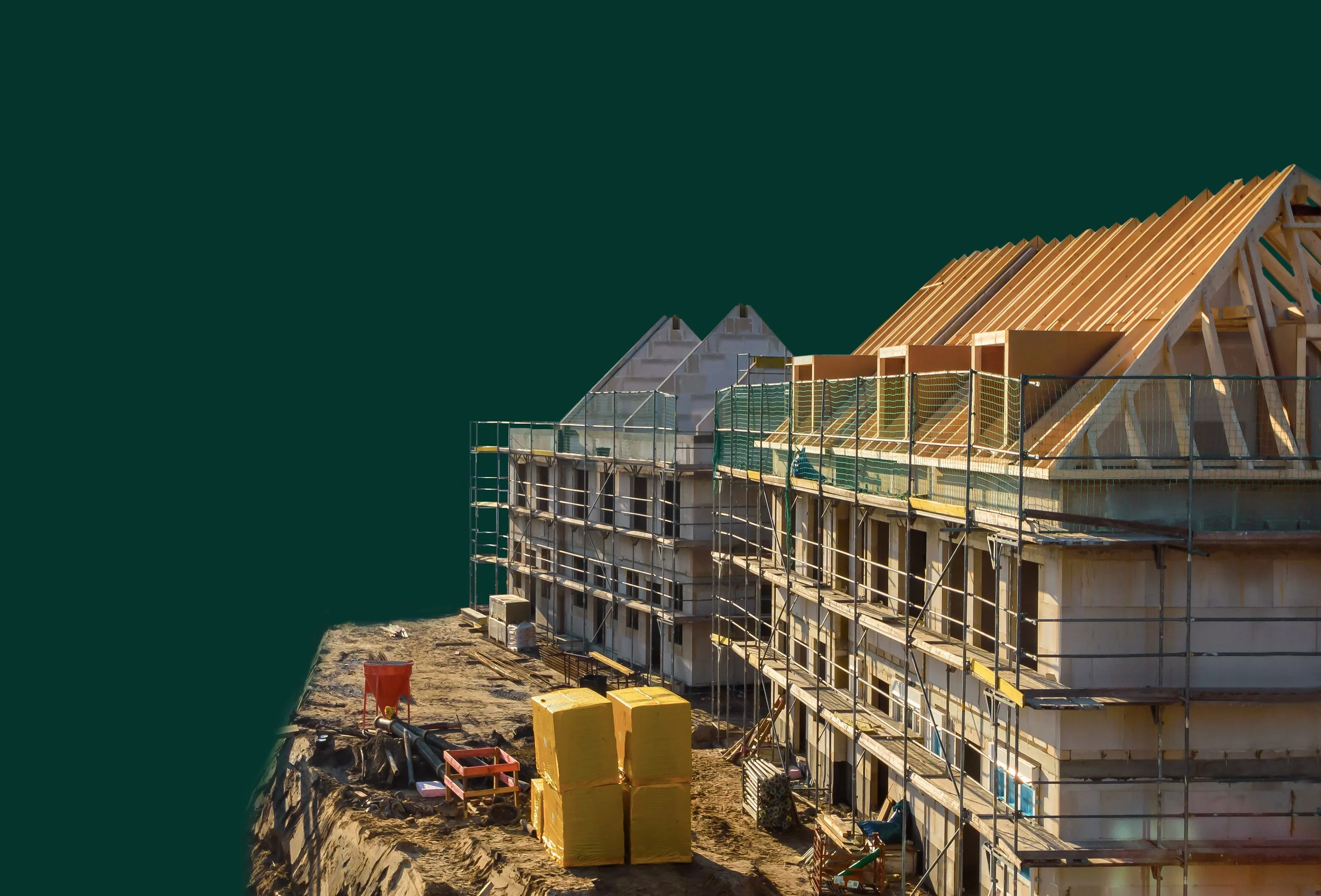 Construction site of a multi-story building with wooden roof framing, scaffolding, and construction materials on the ground.