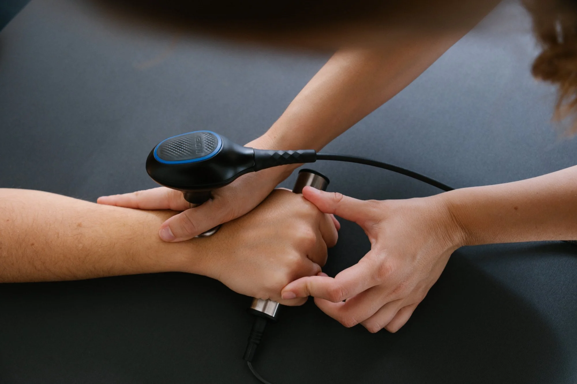 Terapista realiza terapia de electroestimulación a un paciente, aplicando corrientes eléctricas en la pierna del paciente.