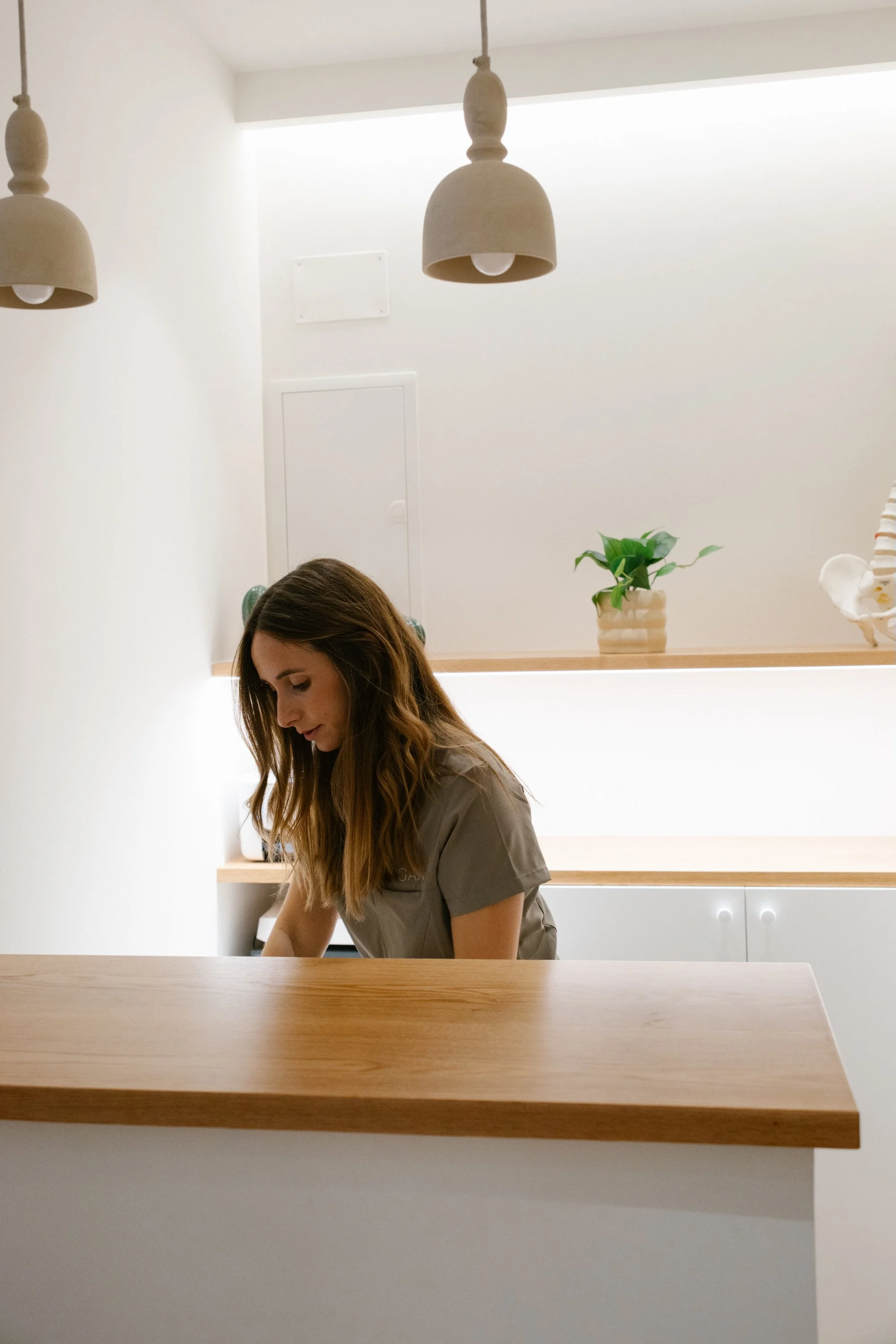 Una mujer con uniforme gris en un espacio interior minimalista y luminoso, con plantas y decoración sencilla.