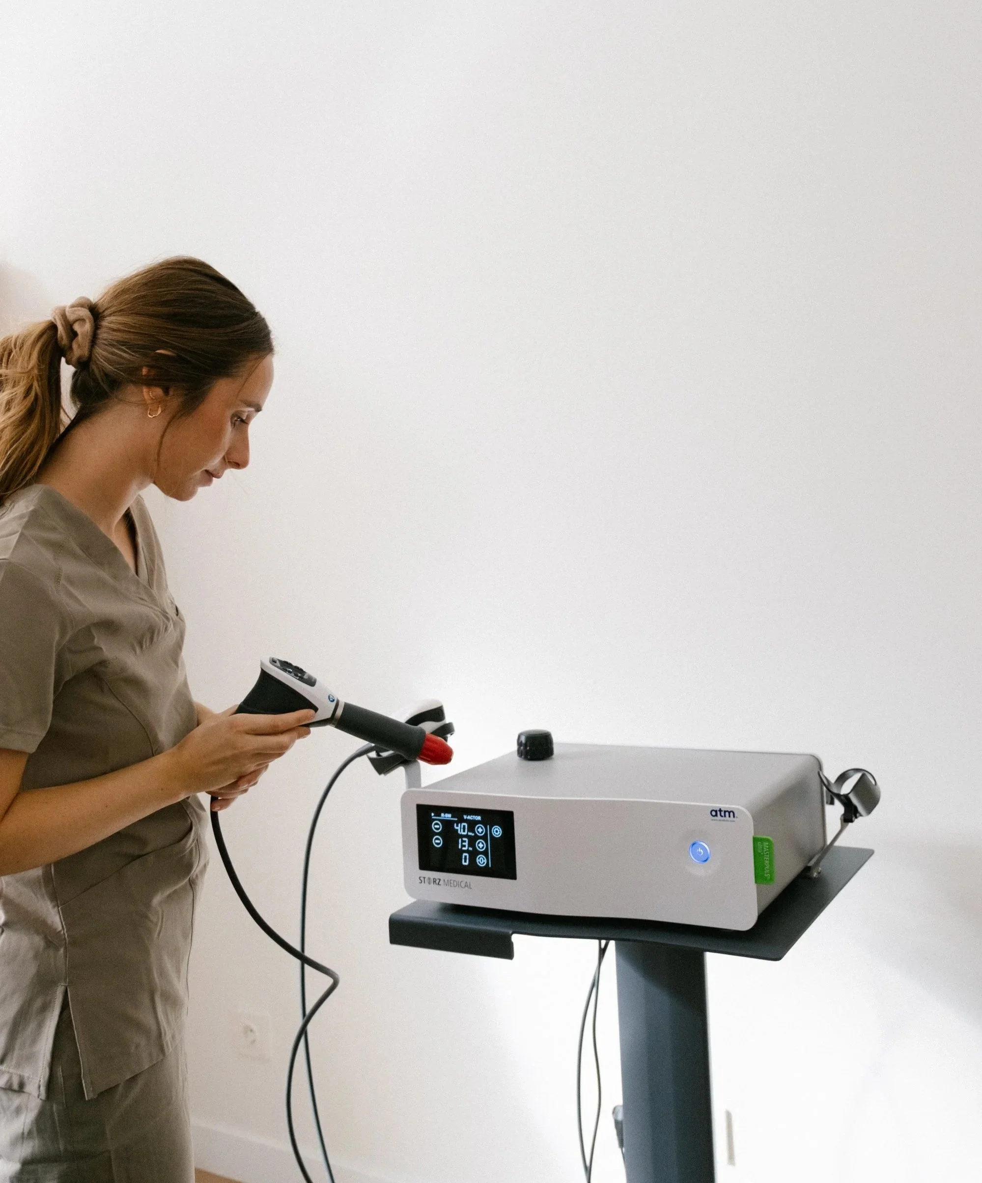 Mujer usando un equipo médico en un consultorio, ajustando un dispositivo en una mesa con pantalla digital