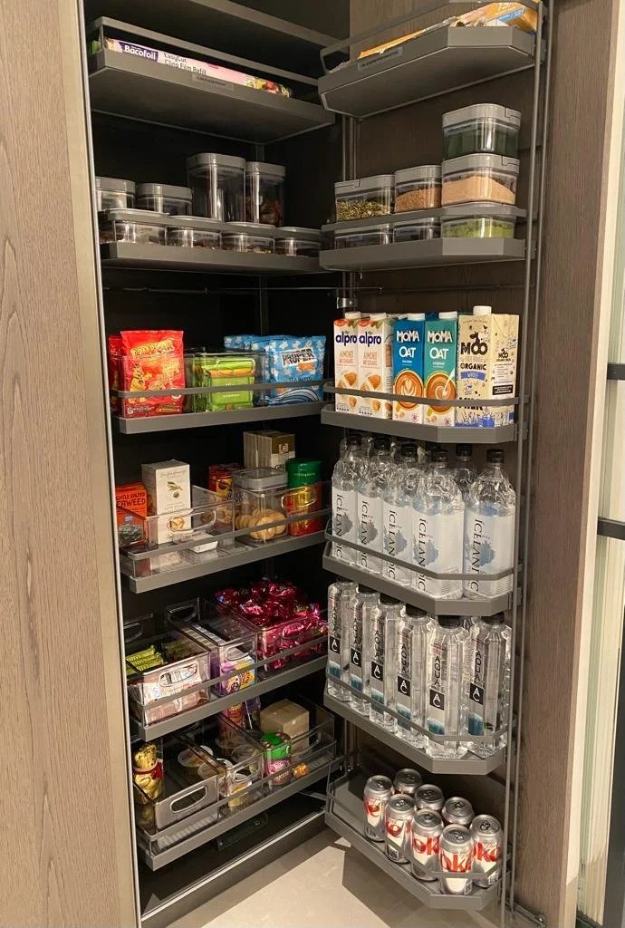 A pantry with various snacks, drinks, and food containers organized on shelves and pull-out trays.