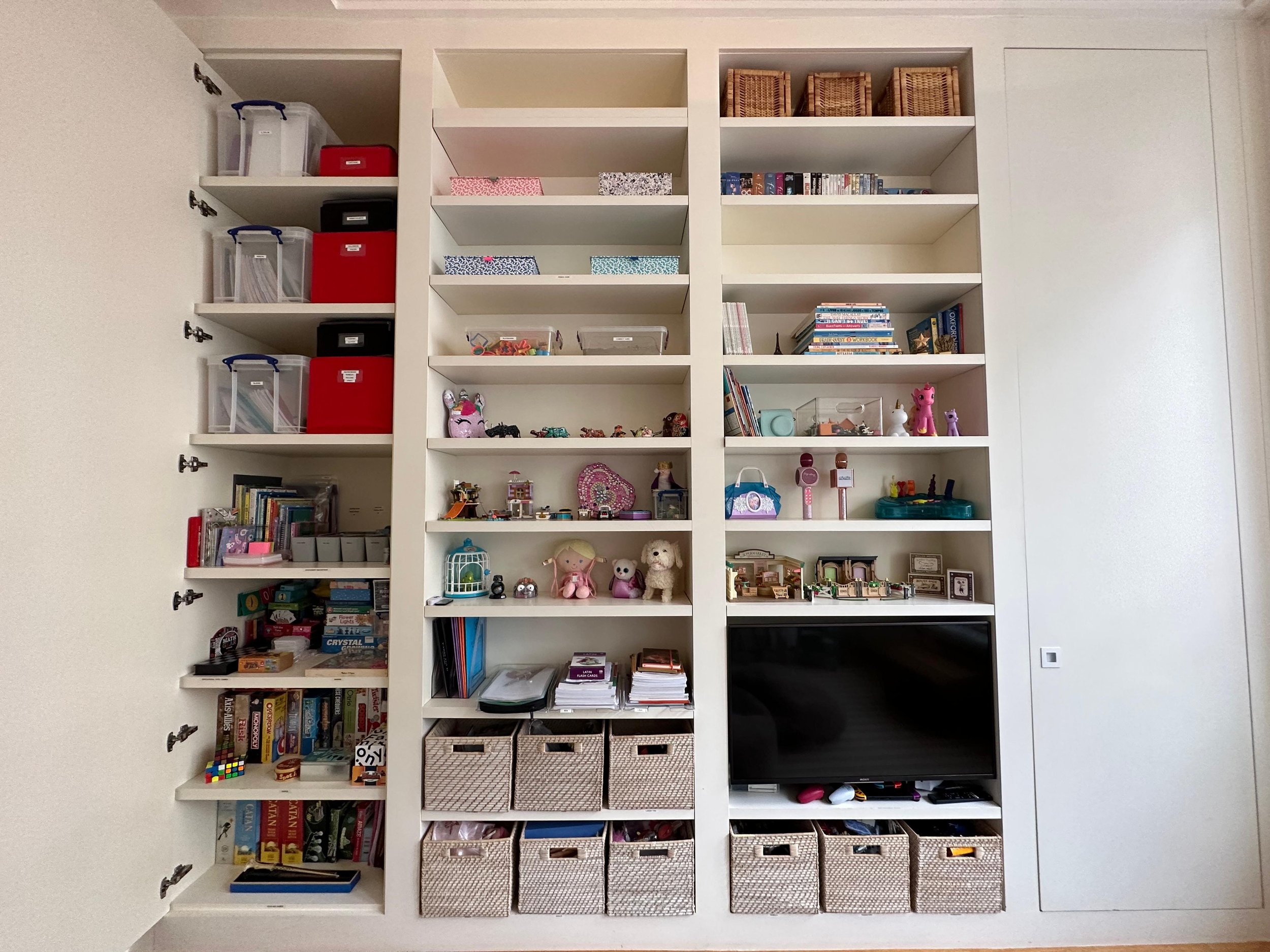 White built-in shelving unit with multiple compartments filled with books, toys, baskets, and decorative items.