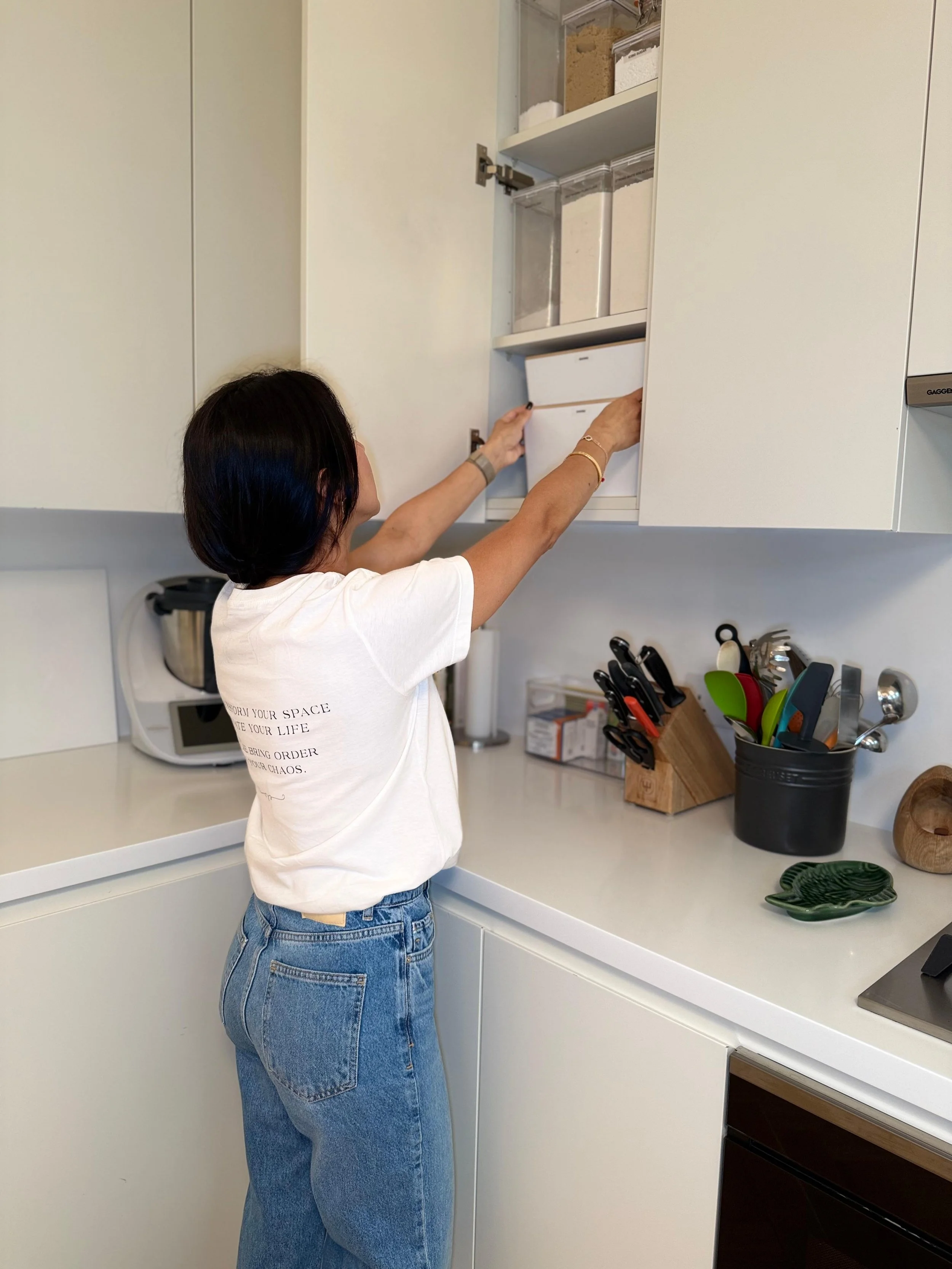 A woman opening an upper kitchen cabinet.
