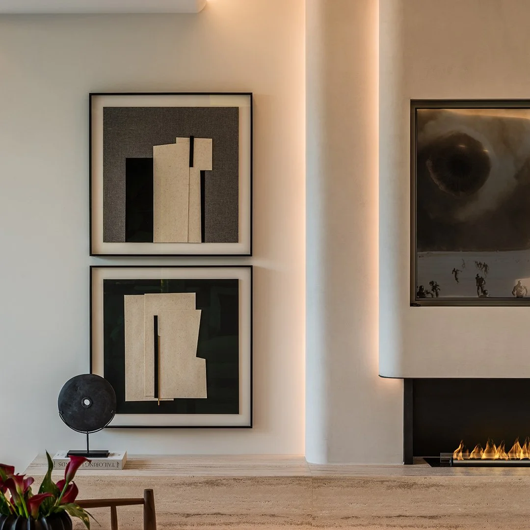 Interior of a modern living room with two abstract art pieces on the wall, a decorative speaker on a book, and a fireplace with a fire burning.