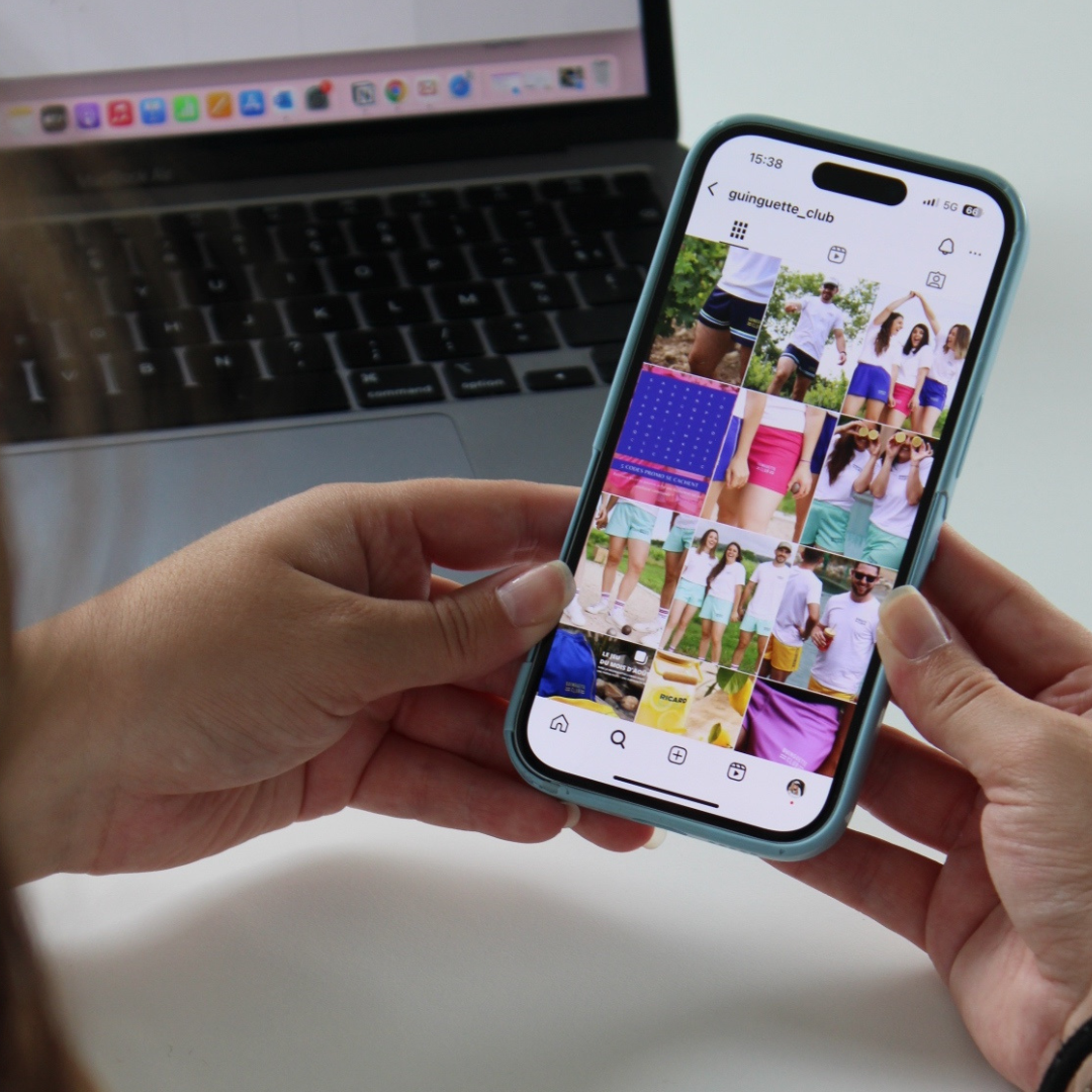 Person tenant un téléphone affichant un profil Instagram nommé 'guinguette_club' avec des photos de groupe d'amis en tenue d'été, portant principalement des shorts et t-shirts, dans différentes activités en extérieur.
