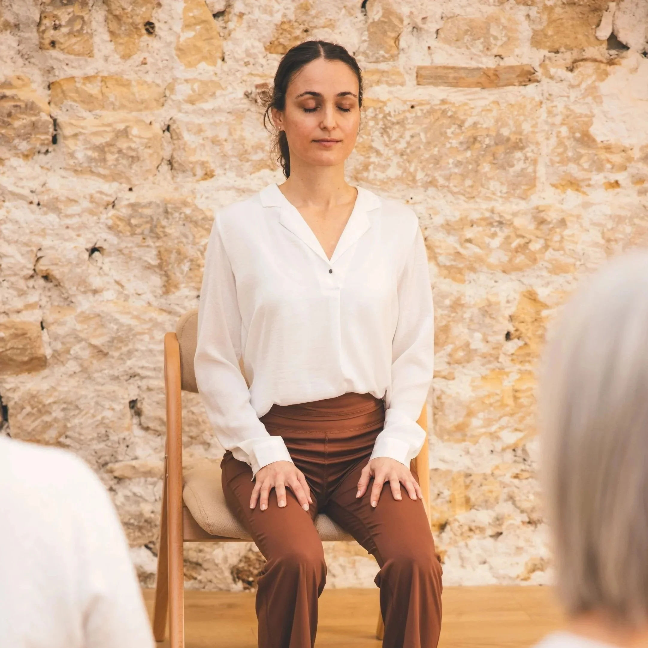 Femme assise sur une chaise, les yeux fermés et les mains sur les genoux, lors d’une pause de yoga au travail