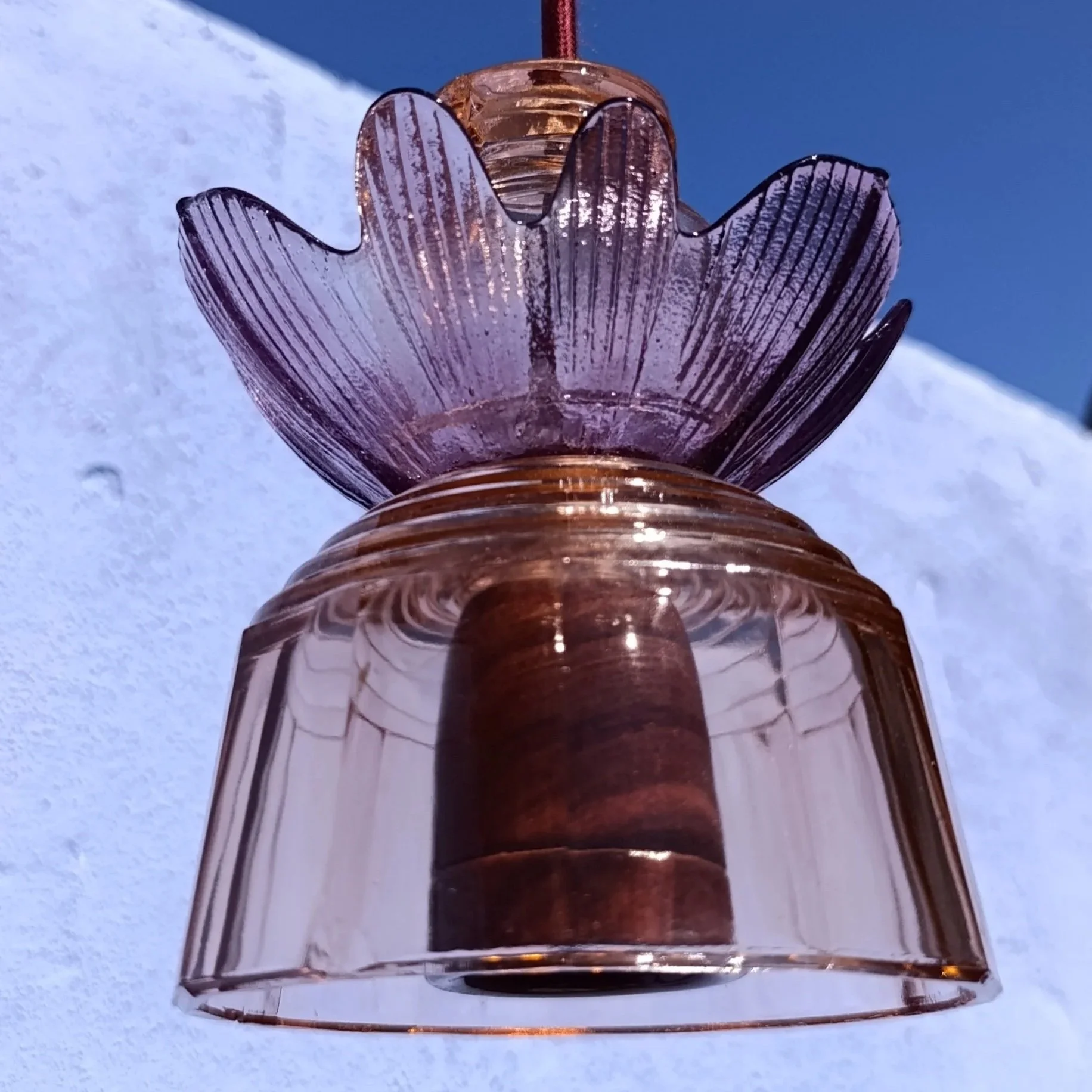 Lanterne en verre rose avec un motif de fleur, suspendue contre un fond de ciel bleu et de neige.