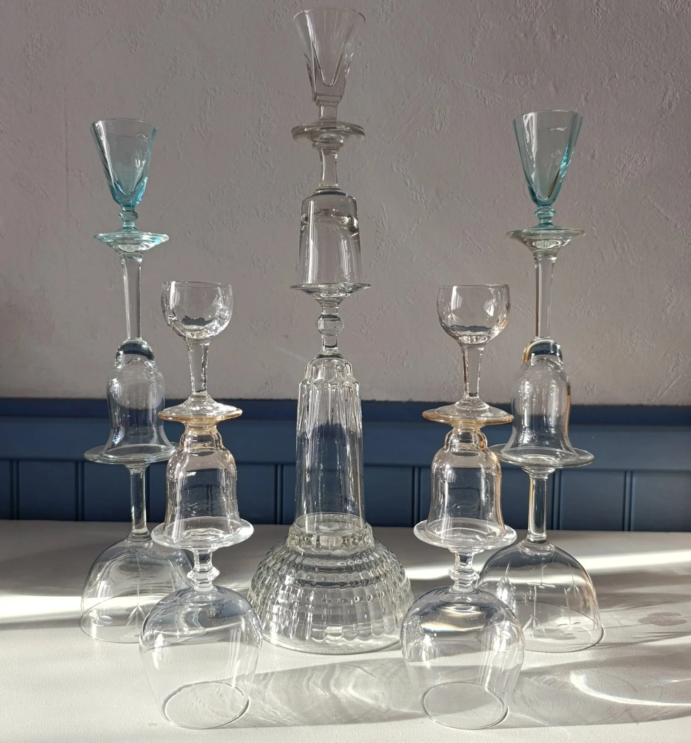 Verre en verre empilés formant une sculpture géométrique sur une table, avec un fond en mur blanc et plinthes bleues