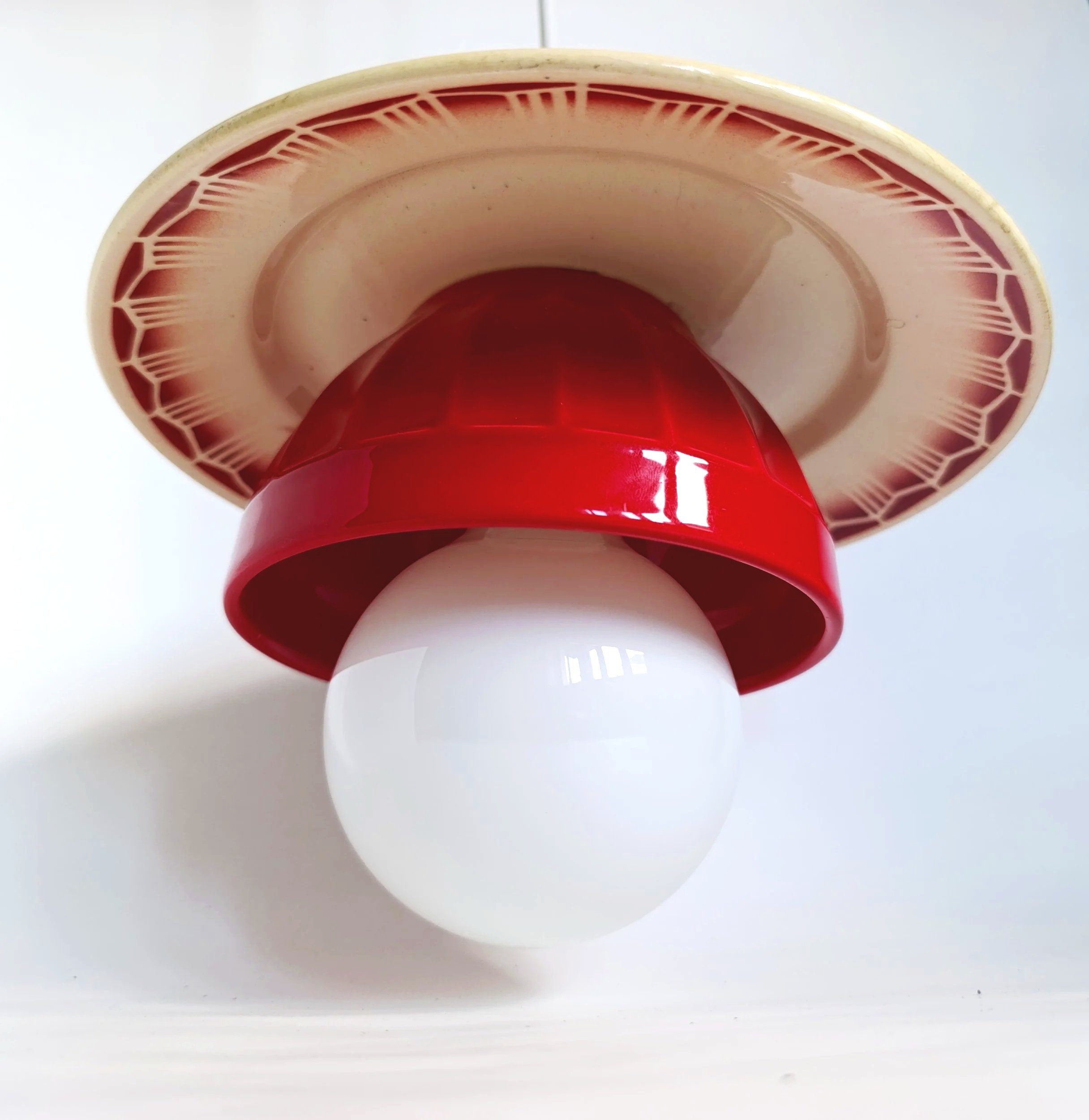 L'objet en forme de lampe ou de sculpture artistique avec une base sphérique blanche, une section centrale rouge et une partie supérieure jaune avec un motif en forme de rayures. La photo est prise en dessous, montrant une vue inversée.