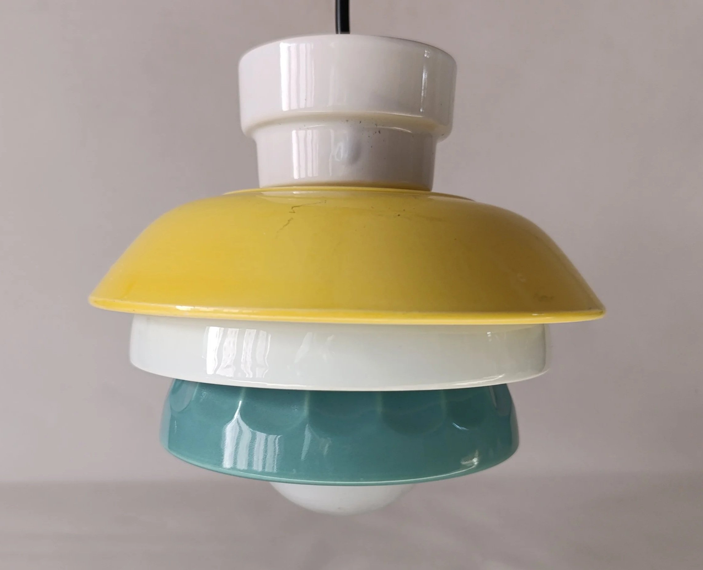 Lampe suspendue composée de plusieurs anneaux colorés en jaune, blanc, turquoise et blanc, empilés verticalement.