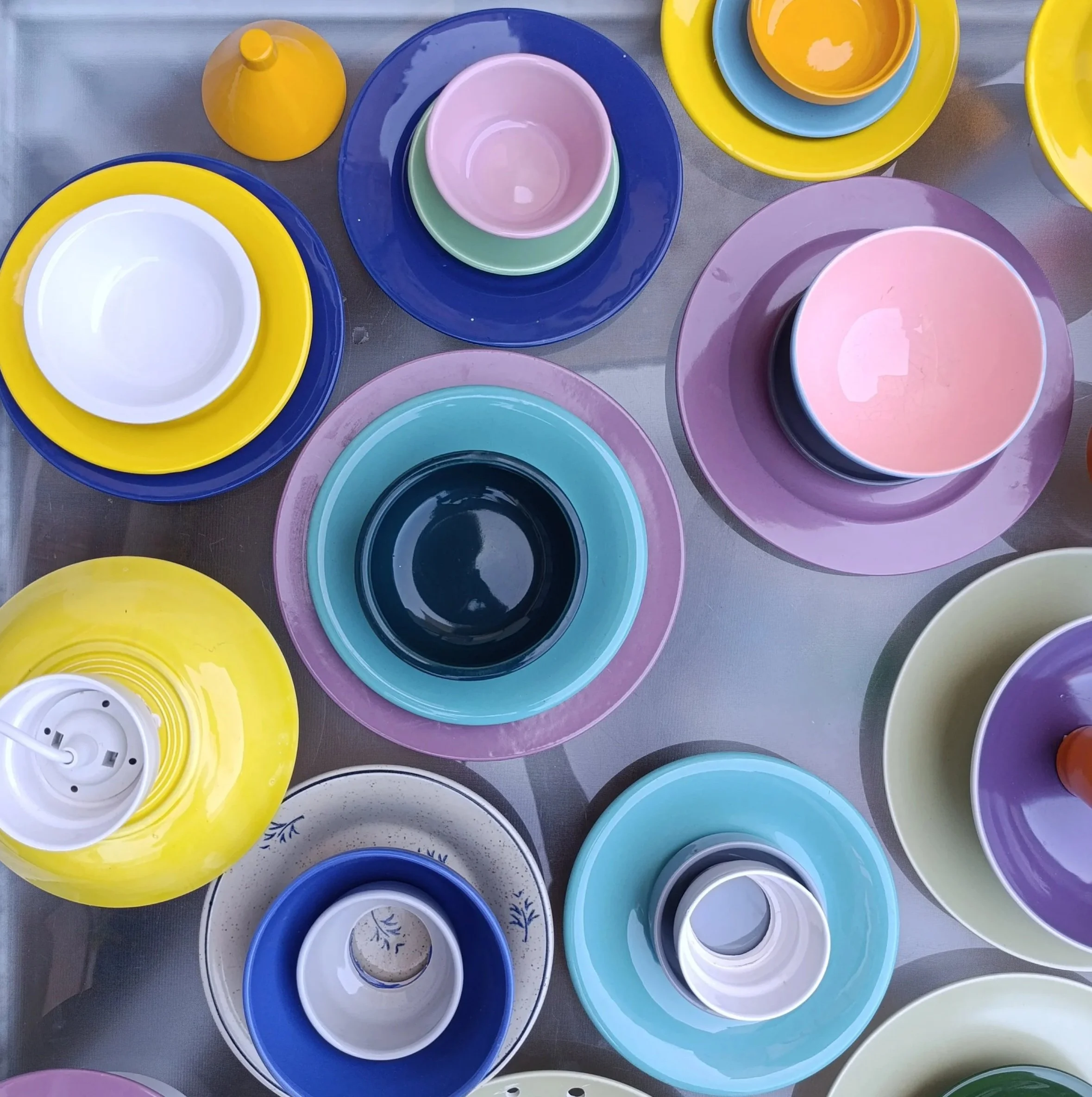 Assortiment de vaisselle en céramique colorée comprenant des assiettes, des bols et des bougeoirs dans différentes couleurs pastel et vives, disposés sur une surface.