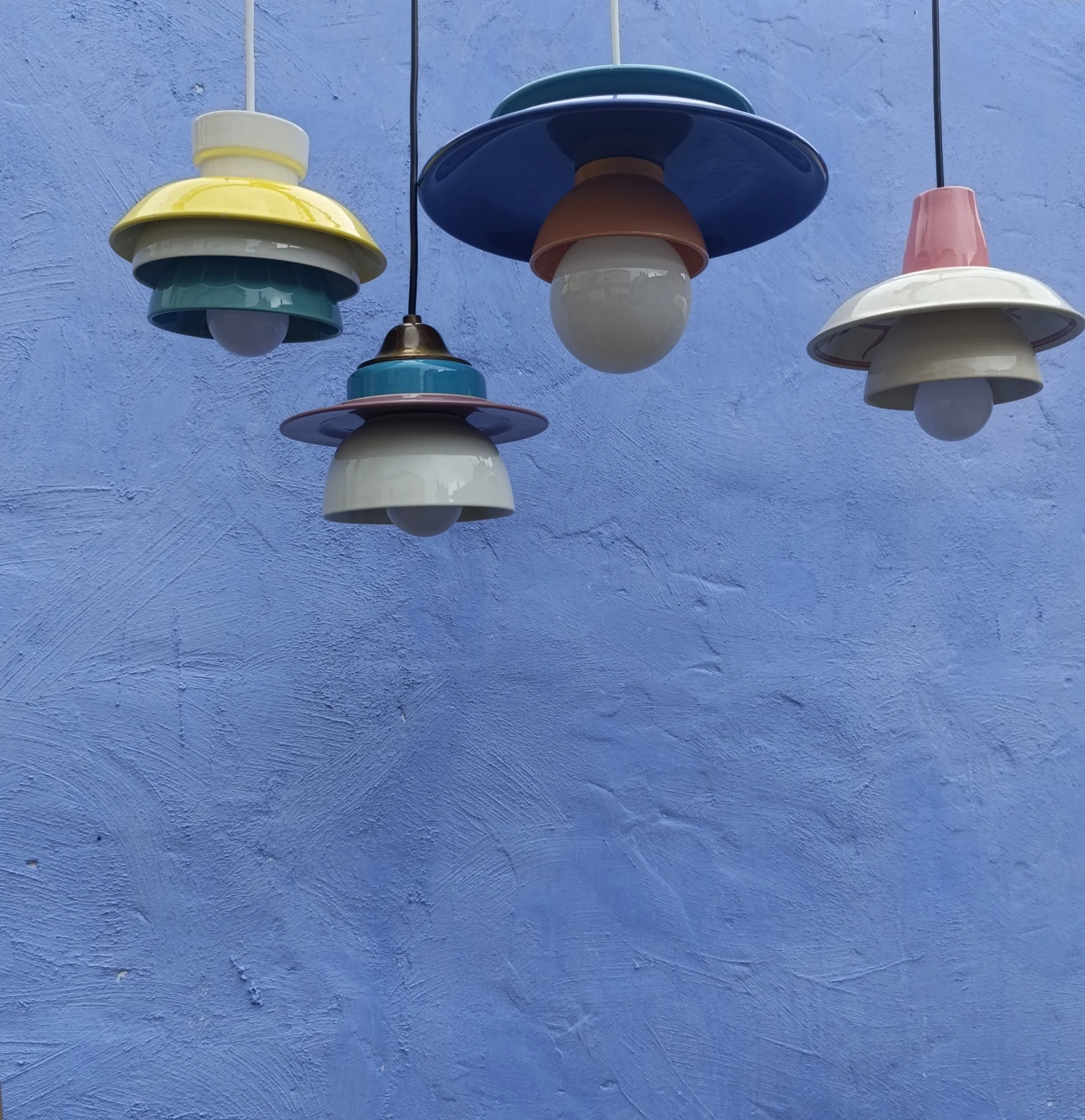 Quatre lampes suspendues de styles modernes colorées contre un mur violet.