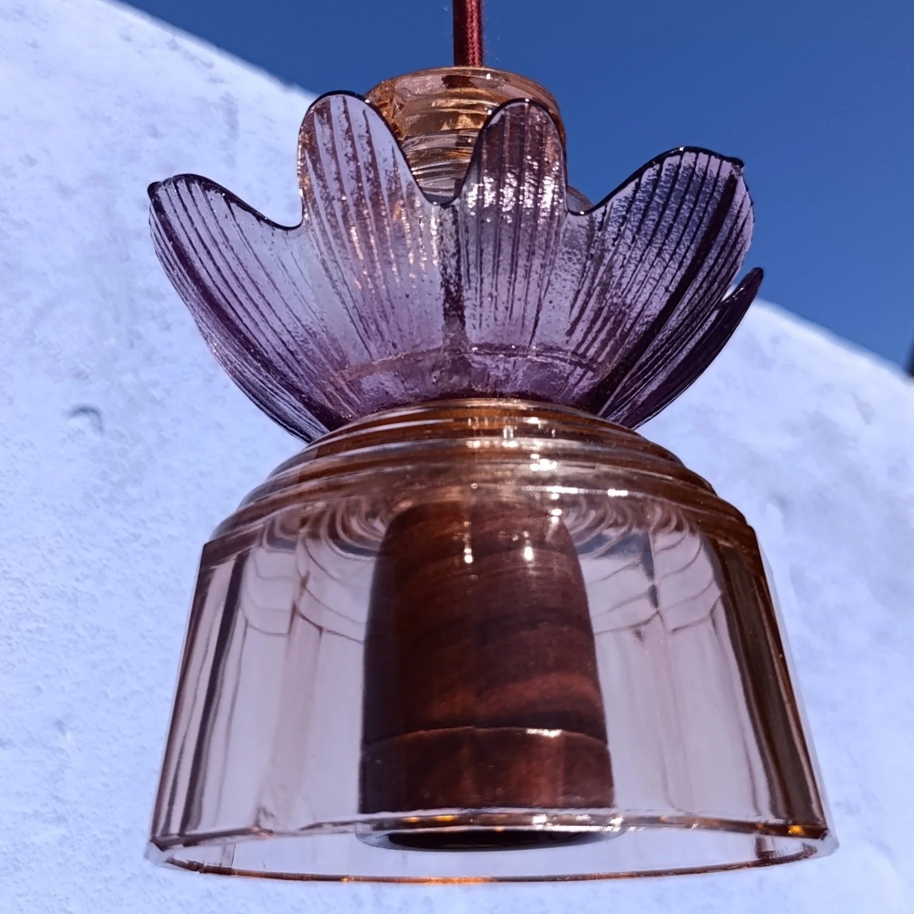 Lanterne en verre translucide à motif floral, suspendue contre un ciel bleu, avec neige au premier plan.