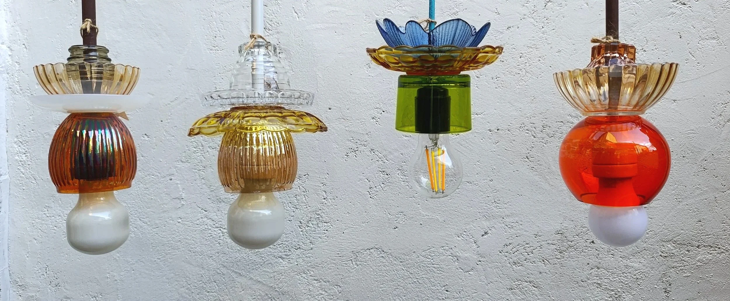 Suspensions upcyclés en verreries chinés coloré suspendues contre un mur blanc crayeux.