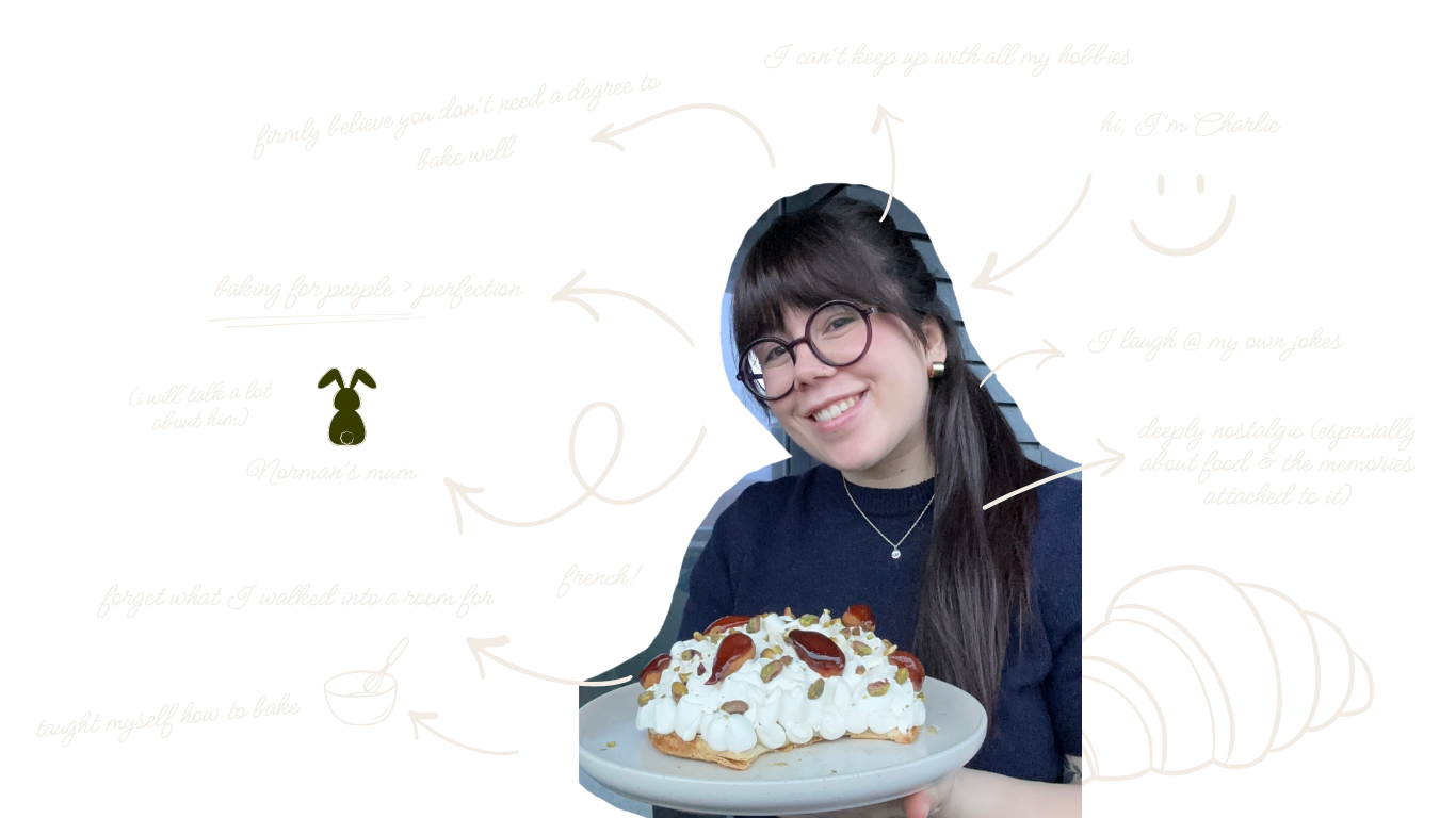 A young woman with glasses and dark hair, smiling, holding a plate with a large cake topped with whipped cream, cherry, and pistachios.