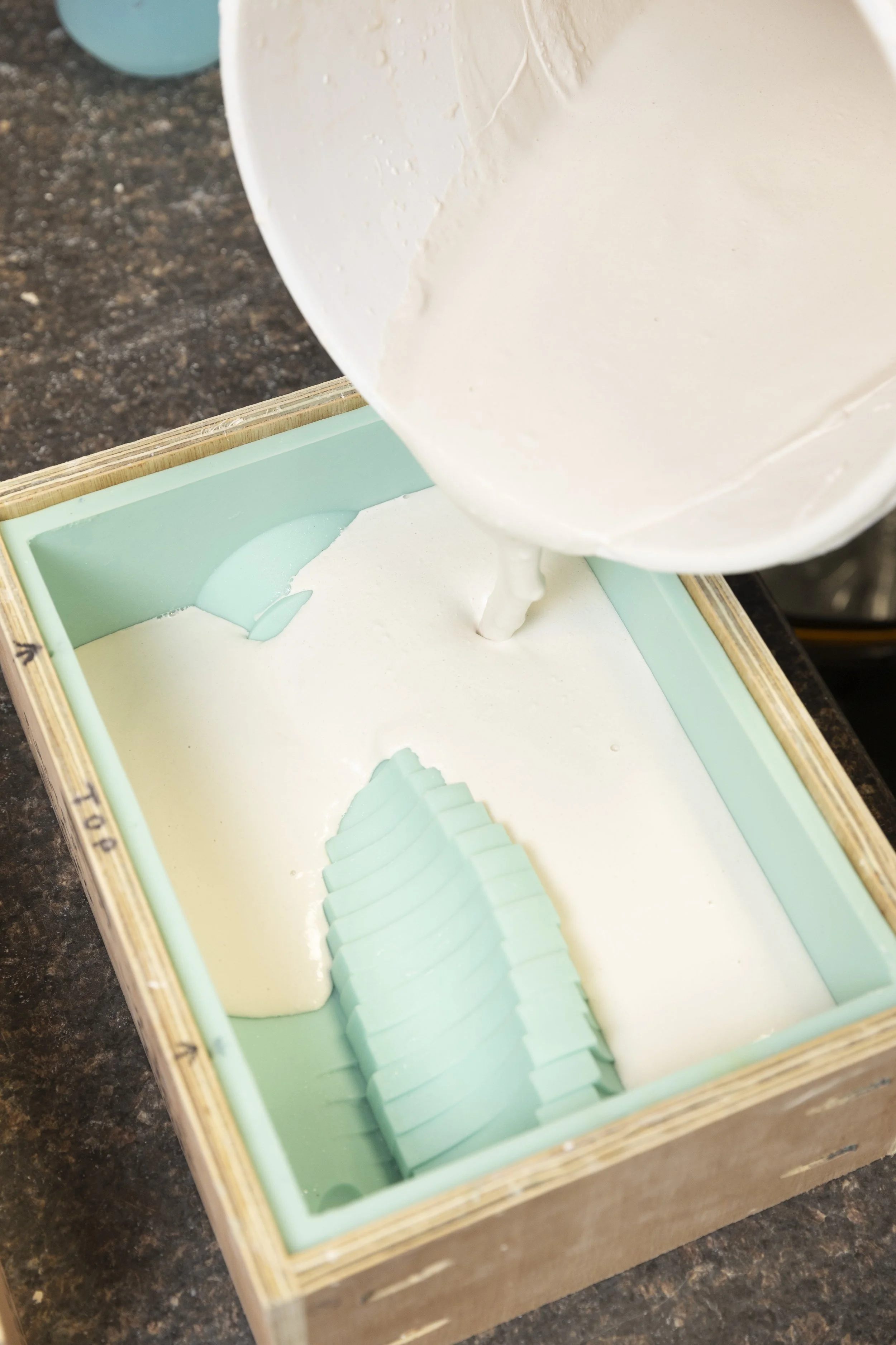 Pouring white soap mixture into a silicone mold with flower-shaped cavities.