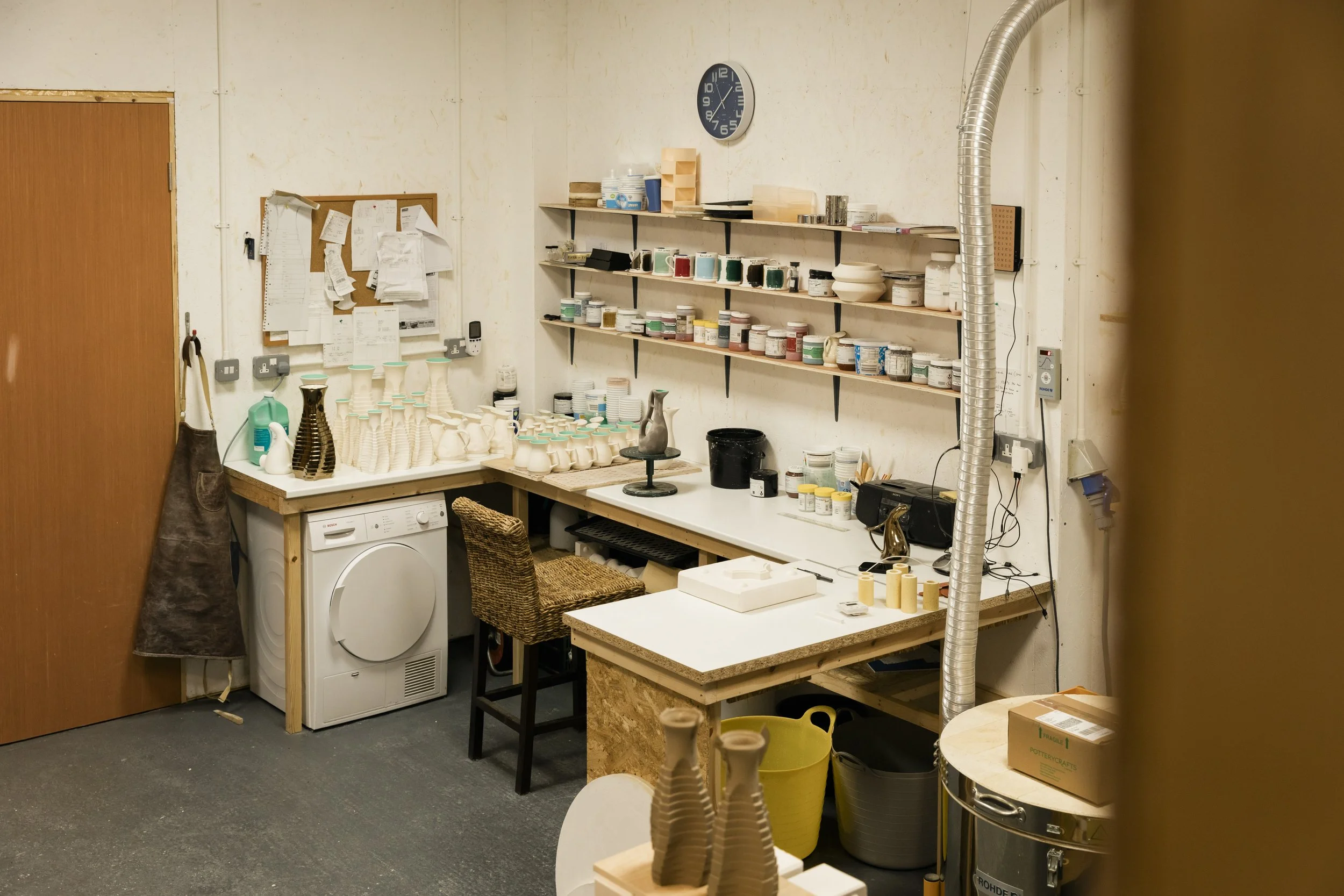 Arra Fletcher's ceramic studio with shelves of glaze and supplies, a work table with ceramics, and various tools and equipment.