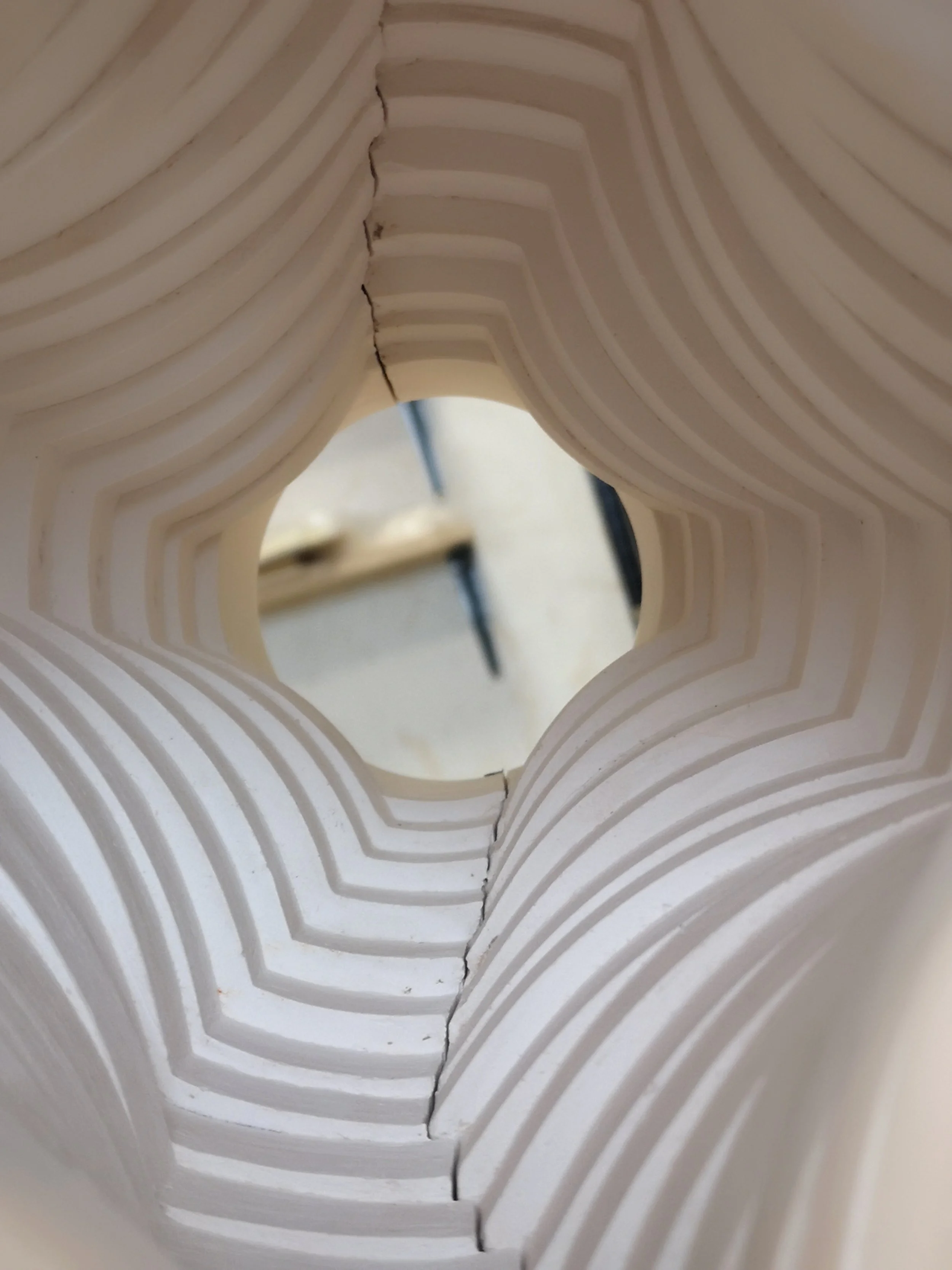Close-up of a hollow, multi-layered, white ceramic object with concentric rectangular cutouts, viewed from the inside.