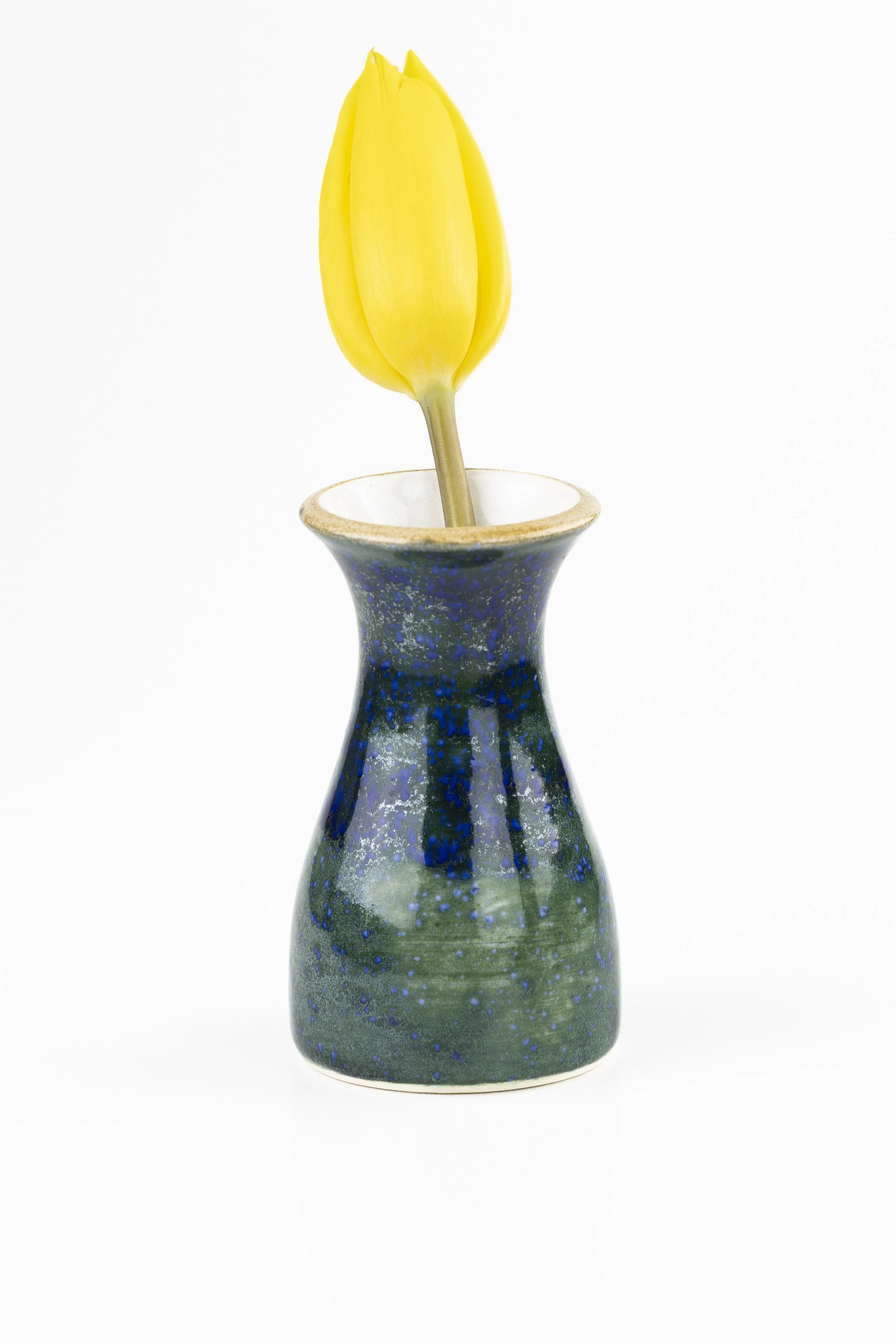 Yellow tulip in a blue speckled ceramic vase against a white background.