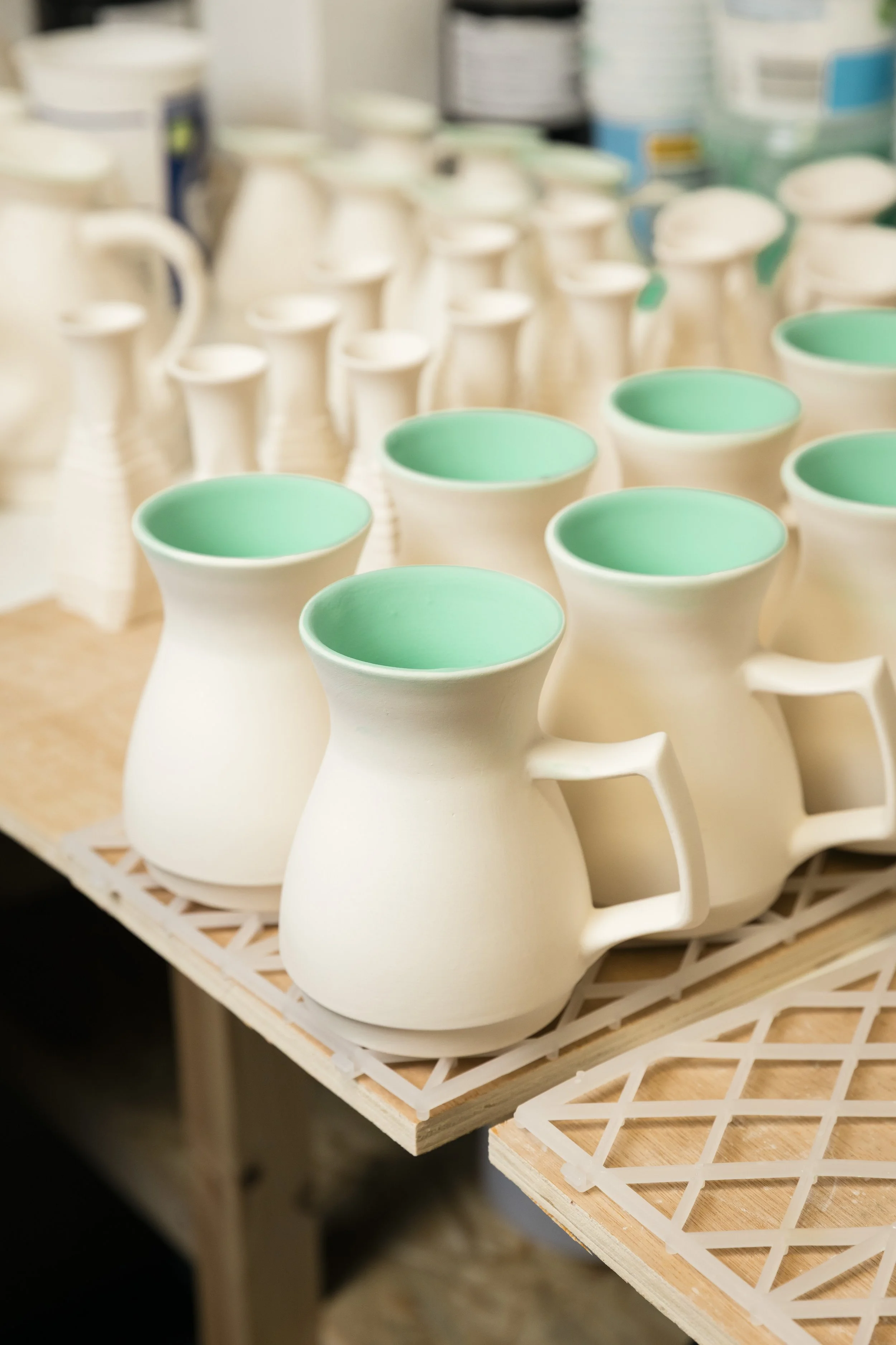 Several unfinished ceramic pitchers with turquoise interiors on a worktable in a pottery studio.