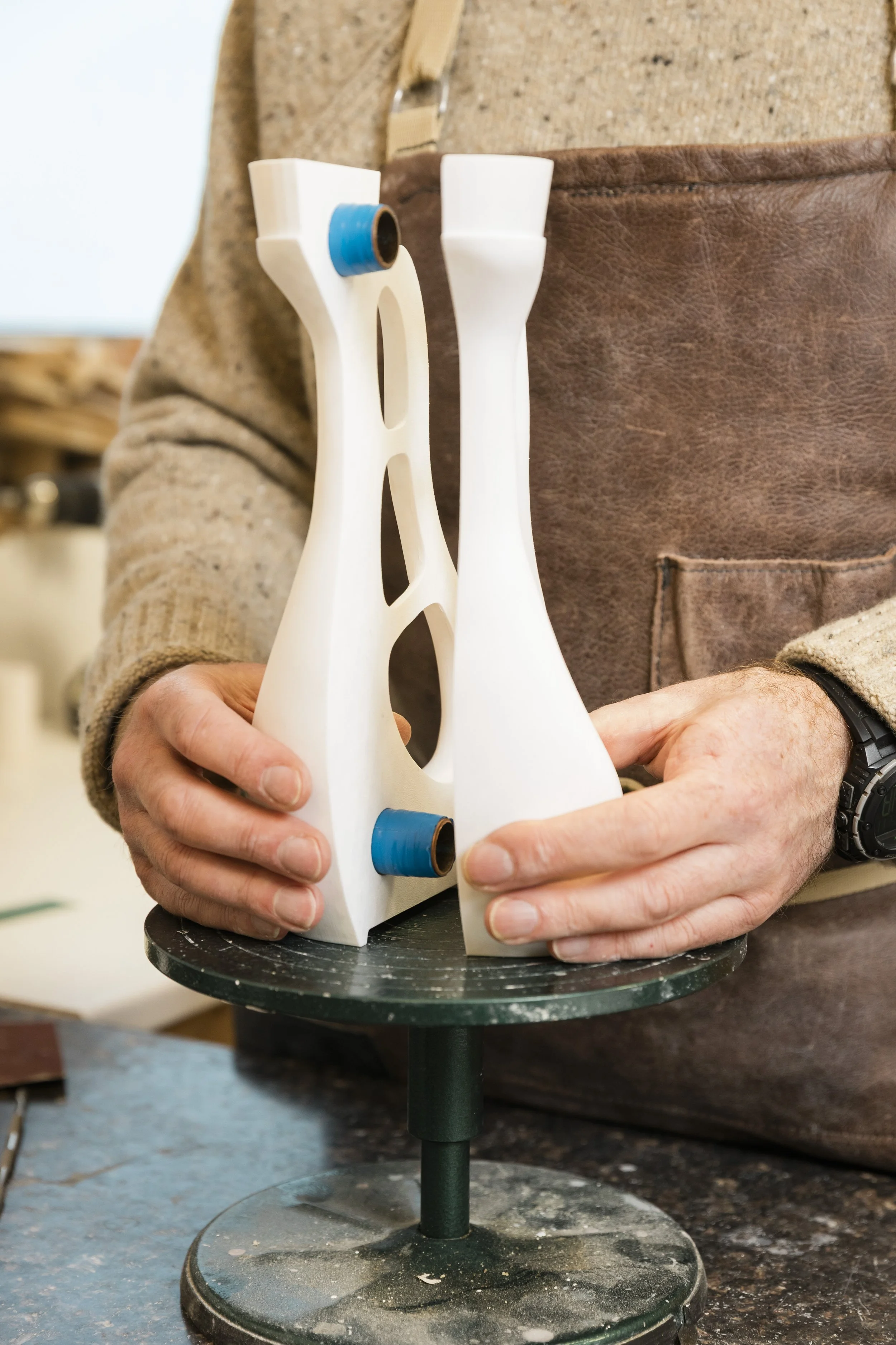 A person holding a white, modern-designed object with blue accents, possibly a sculpture or part of a craft project, on a round black stand.