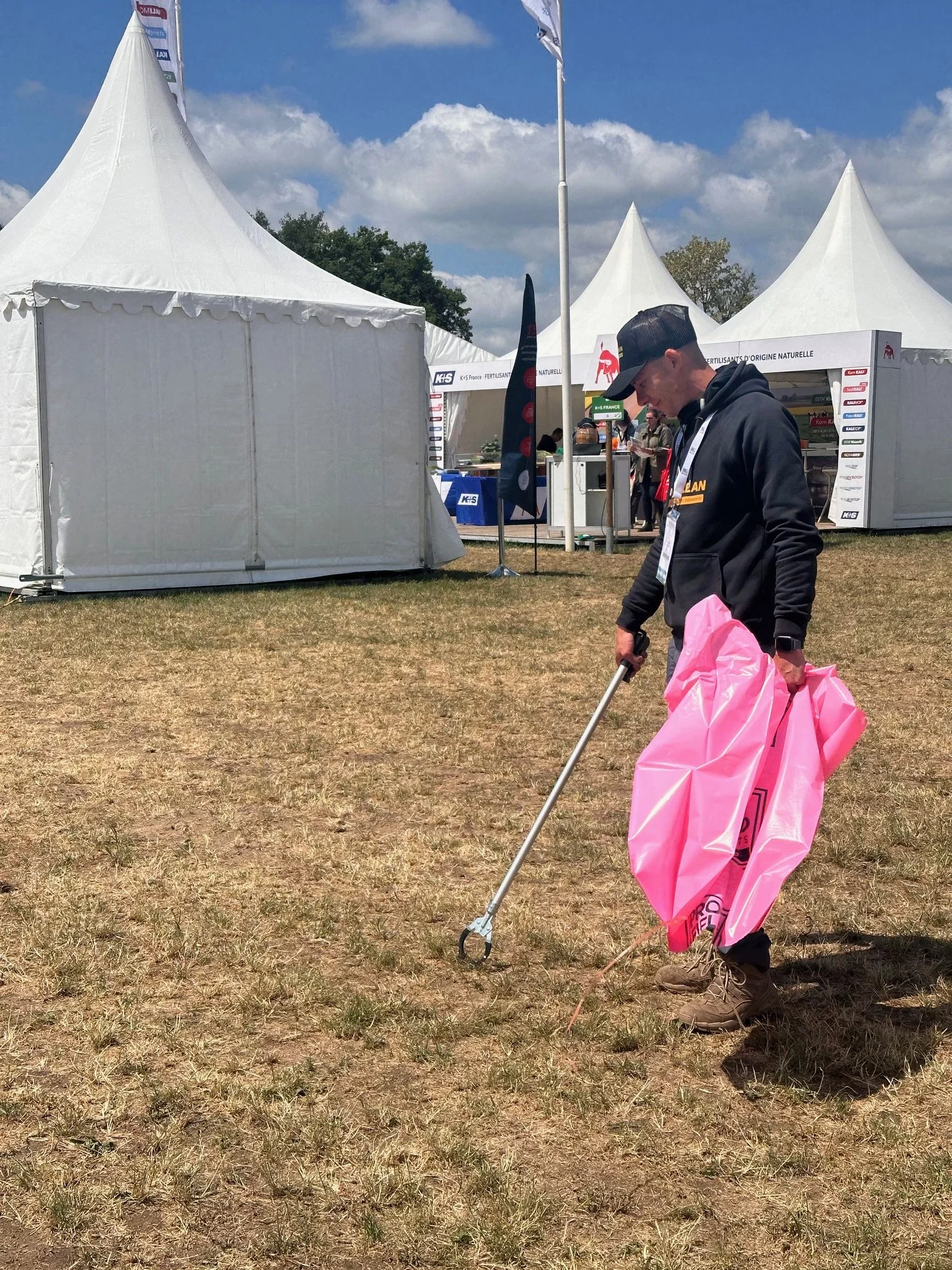 Un employé de AD Clean effectue un ramassage d'ordures à la pince sur un évènement en extérieur en tenant un sac poubelle rose à la main
