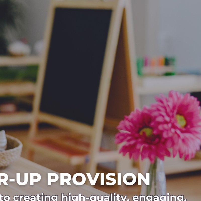 A blurred chalkboard easel with a wooden frame and a bouquet of pink flowers in a glass vase on a table in a classroom or office setting.