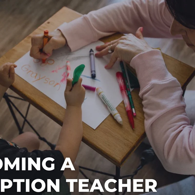Two children and an adult drawing on a white sheet of paper with colored markers at a wooden table.