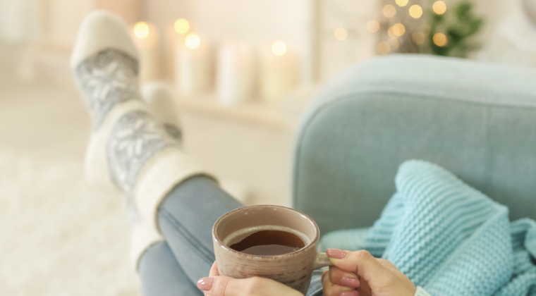 Hands of woman holding cup of tea, with Christmas songs on and calming background