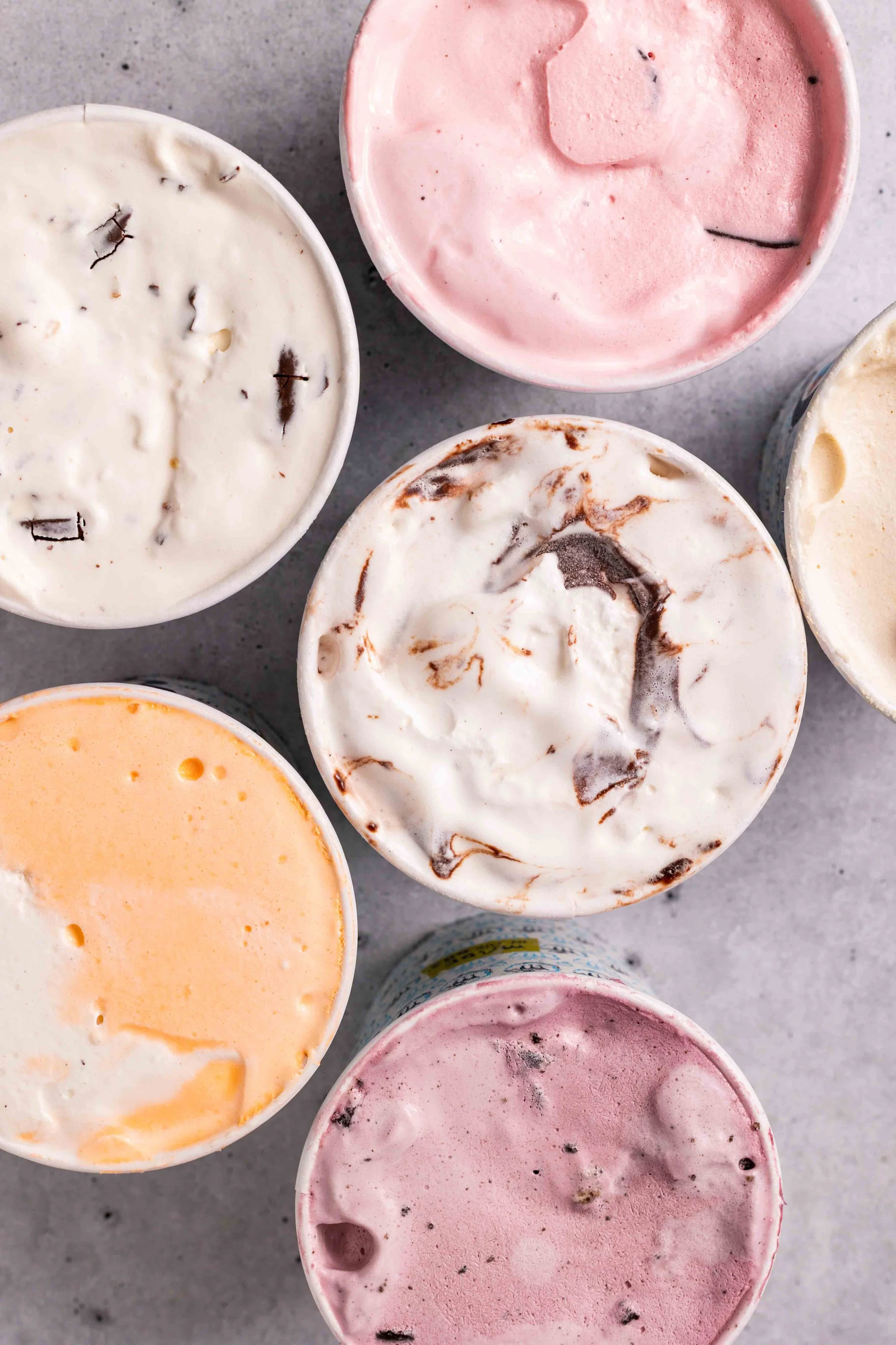 Top view of six small cups of different ice cream flavors on a gray surface.