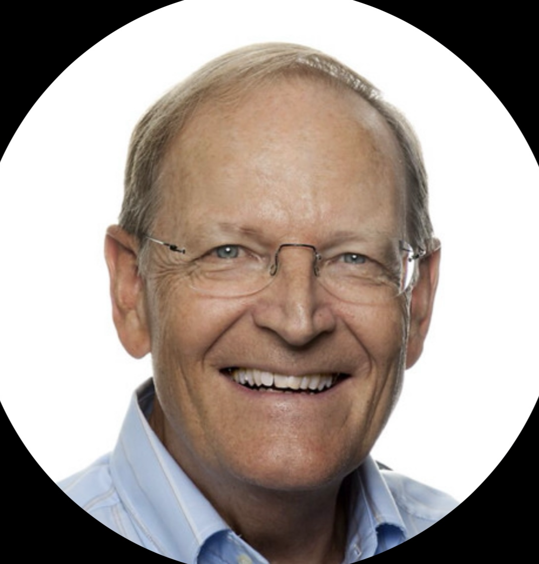 Lächelnder Mann mit Brille, kurz blondes Haar, leicht faltige Haut, trägt einen blauen Hemd an einem weißen Hintergrund.