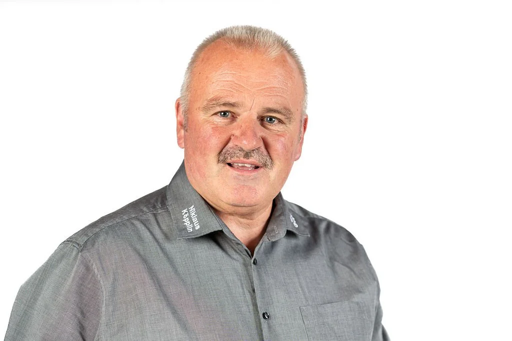 Porträt eines älteren Mannes mit grauem Haar, grauem Hemd vor weißem Hintergrund.