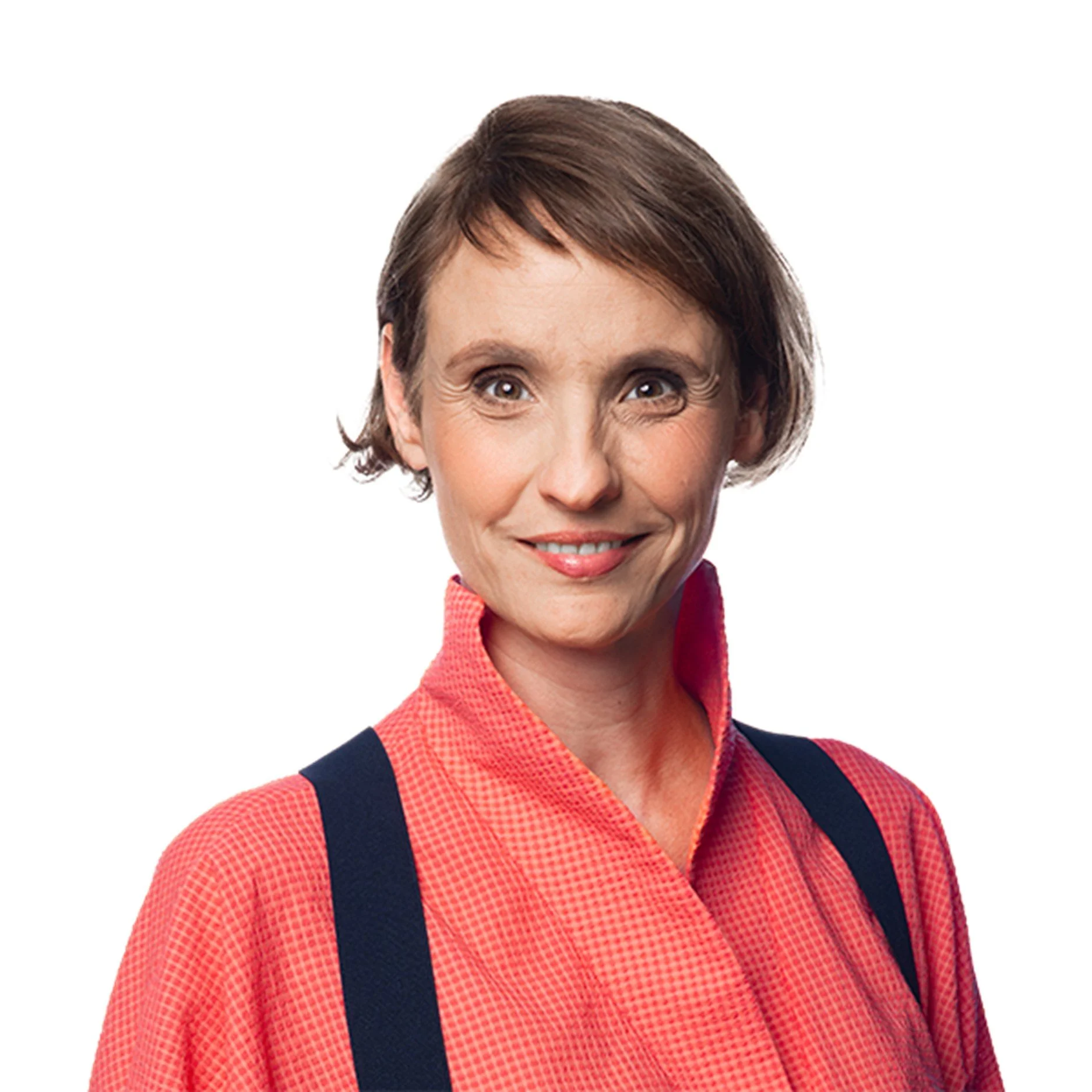 Eine lachende Frau mit kurzen braunen Haaren, trägt einen roten Hemd und schwarze Hosenträger vor weißem Hintergrund.